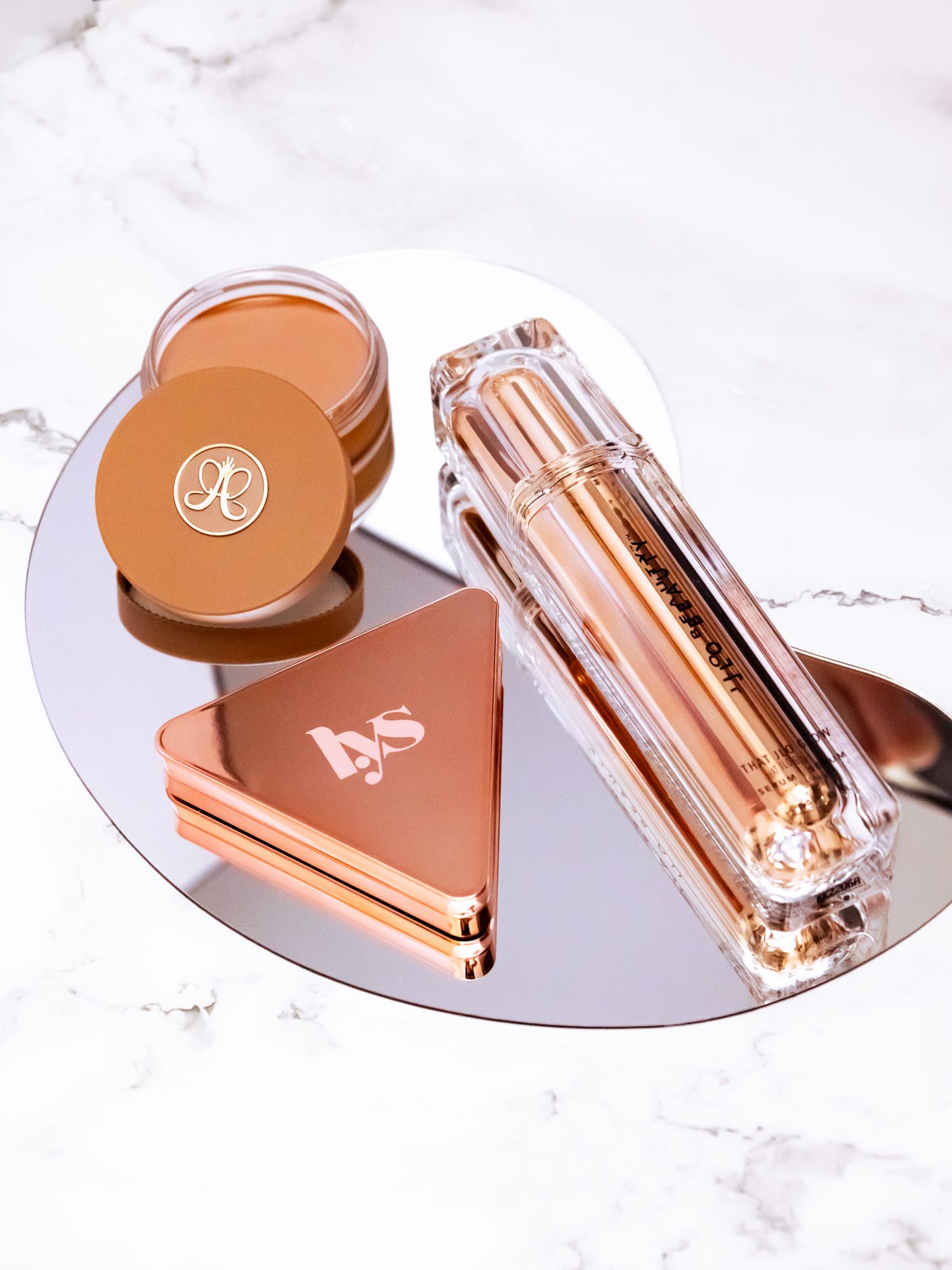Luxury rose gold cosmetic products displayed on circular mirror surface.