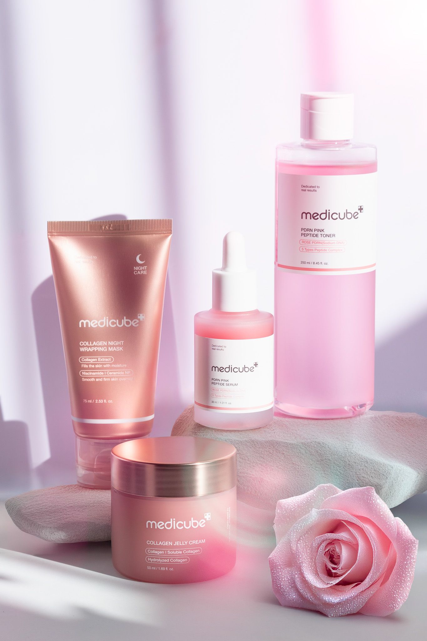 Pink skincare products from Medicube displayed on white surface with pink rose and soft lighting effects.