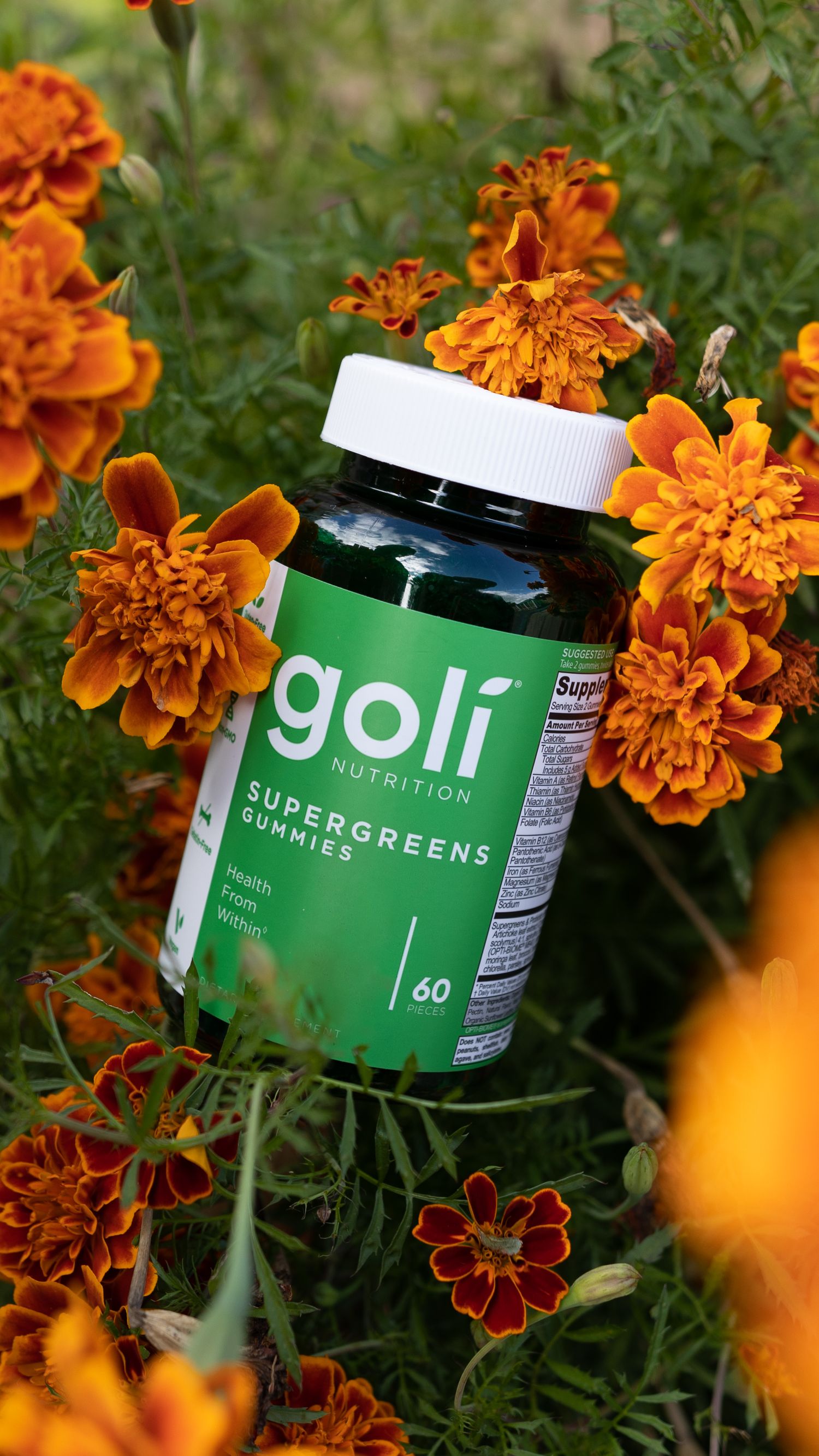 A bottle of Goli Supergreens supplements surrounded by vibrant orange marigold flowers.