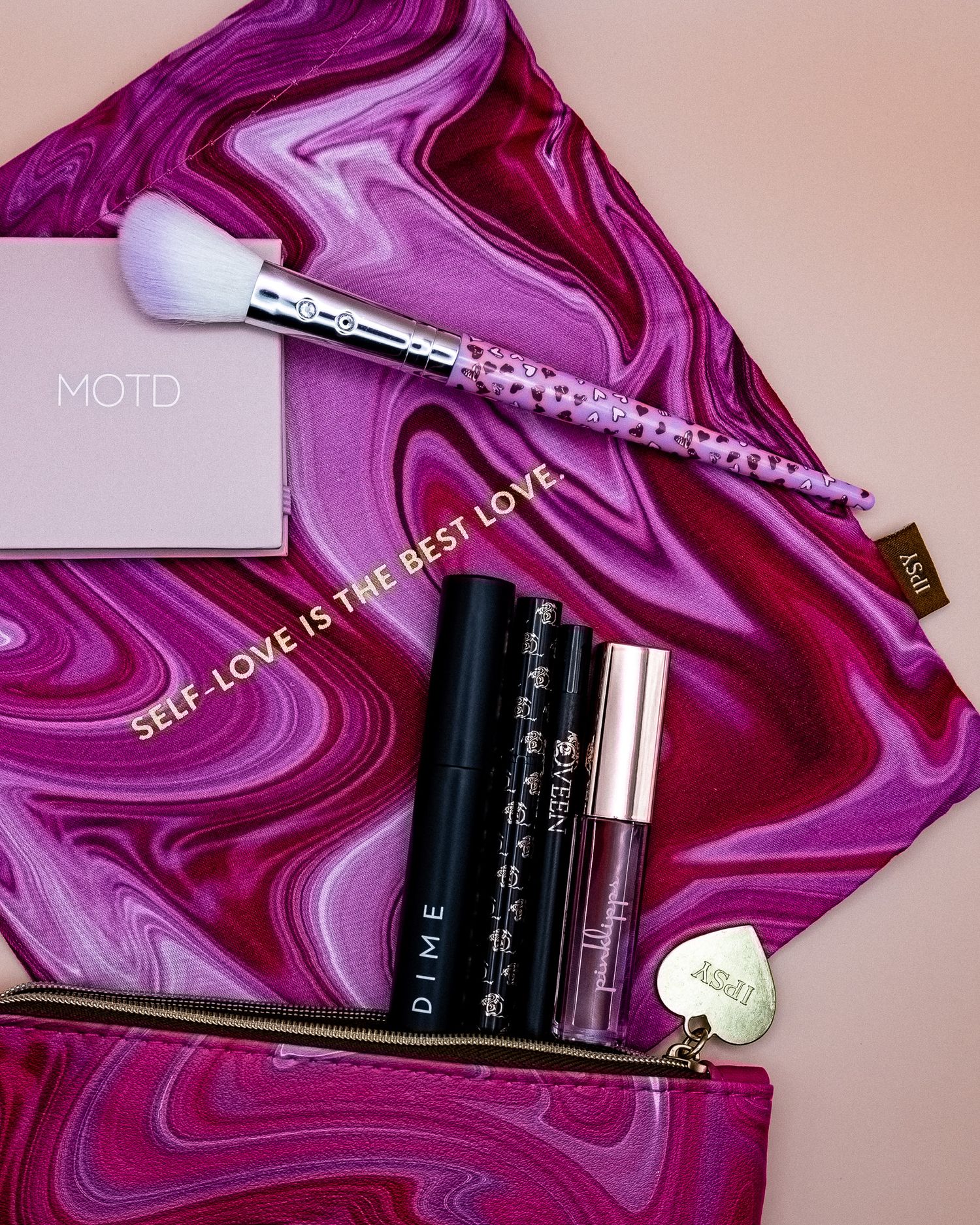 IPSY makeup products and brushes displayed on a swirling purple and pink marble patterned makeup satchel.