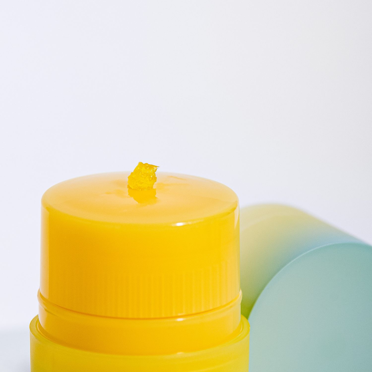 Close-up view of a bright yellow plastic bottle cap against a white background with soft turquoise shadow.