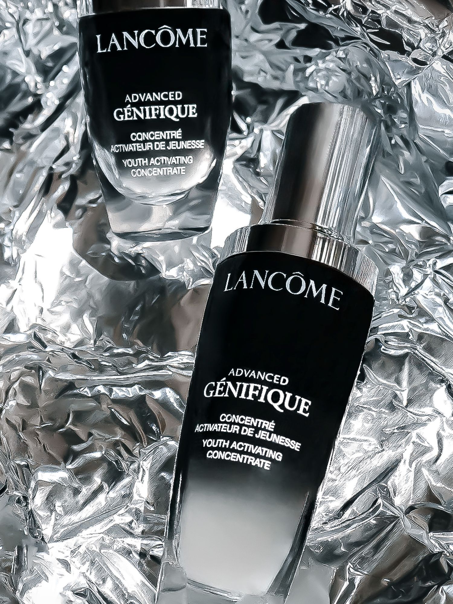 Lancome Genifique skincare products displayed on metallic silver foil background.