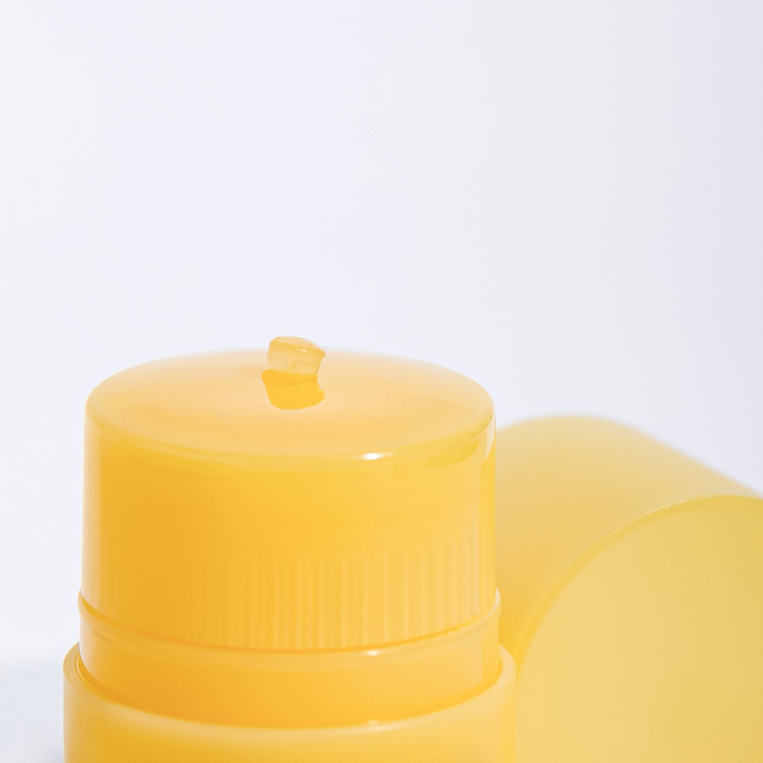 Yellow plastic container with round lid and lipbalm swatch partially visible against white background.