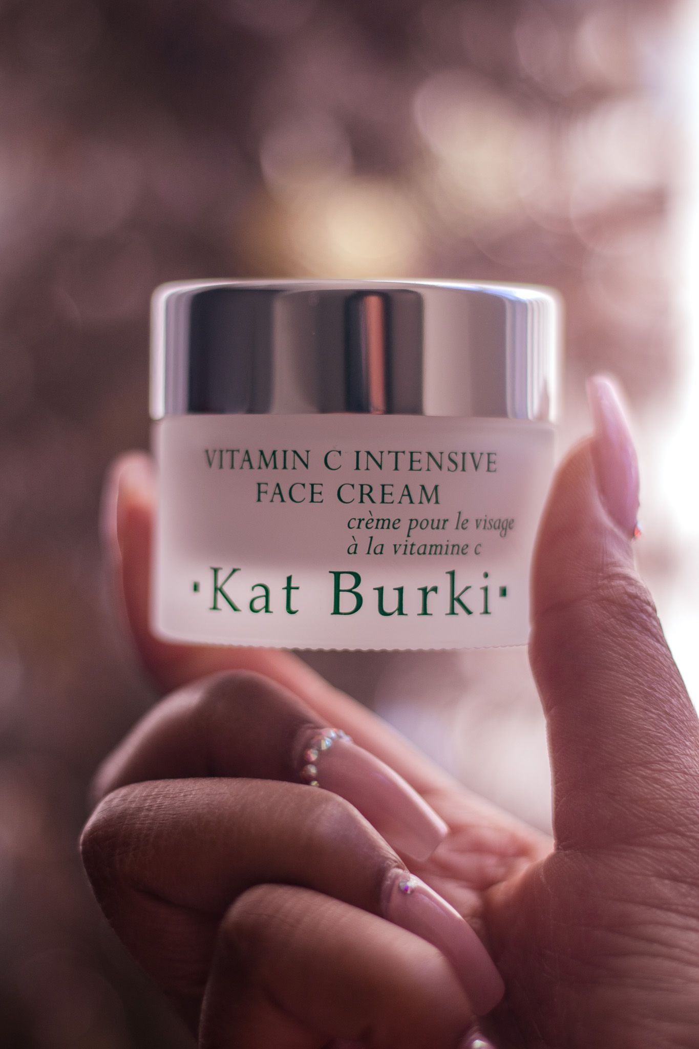 Close-up of Kat Burki Vitamin C face cream jar held in soft focus.