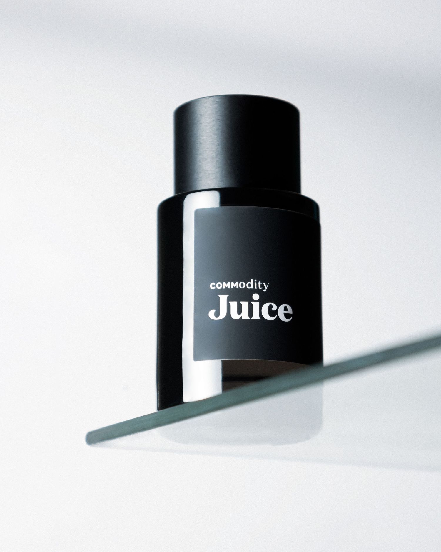 Sleek black bottle of Commodity Juice photographed on minimalist white background.