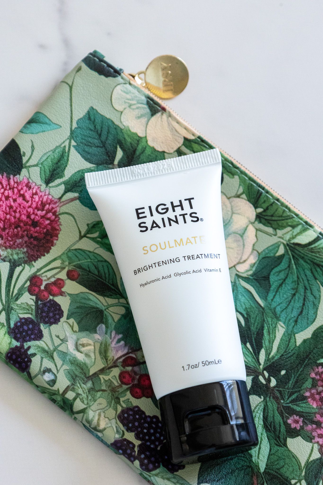 Eight Saints skincare product tube displayed on a floral pattern wallet or clutch with green leaves and pink flowers.