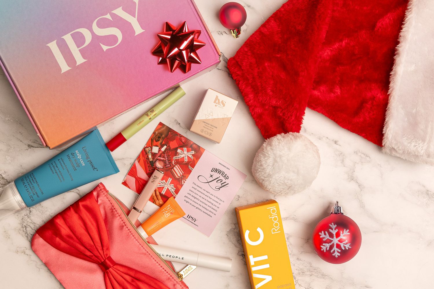 A holiday flatlay with IPSY beauty products, skincare items, and Christmas decorations on a white background.