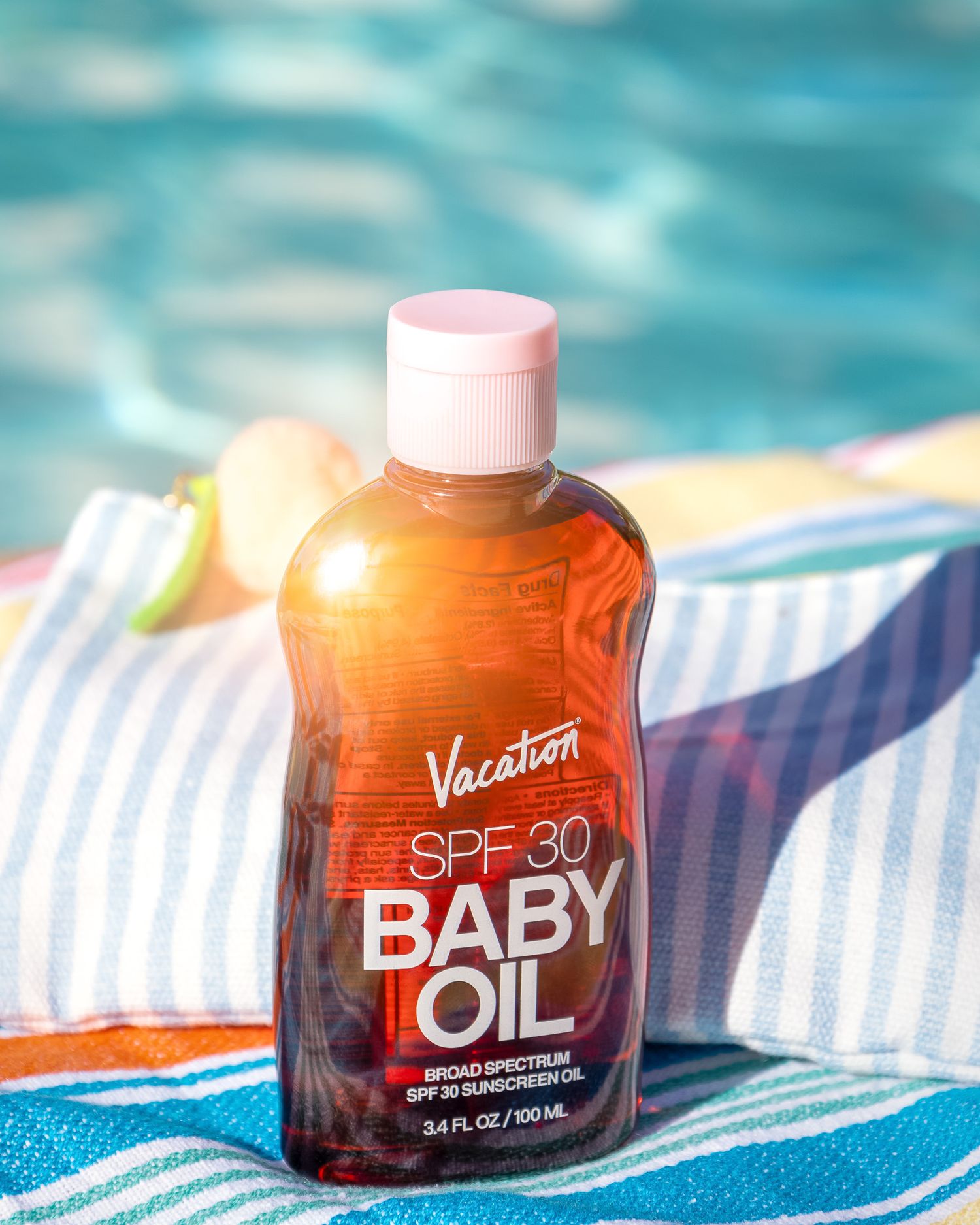 Vacation Baby Oil SPF 30 bottle on striped towel by poolside in sunny setting.