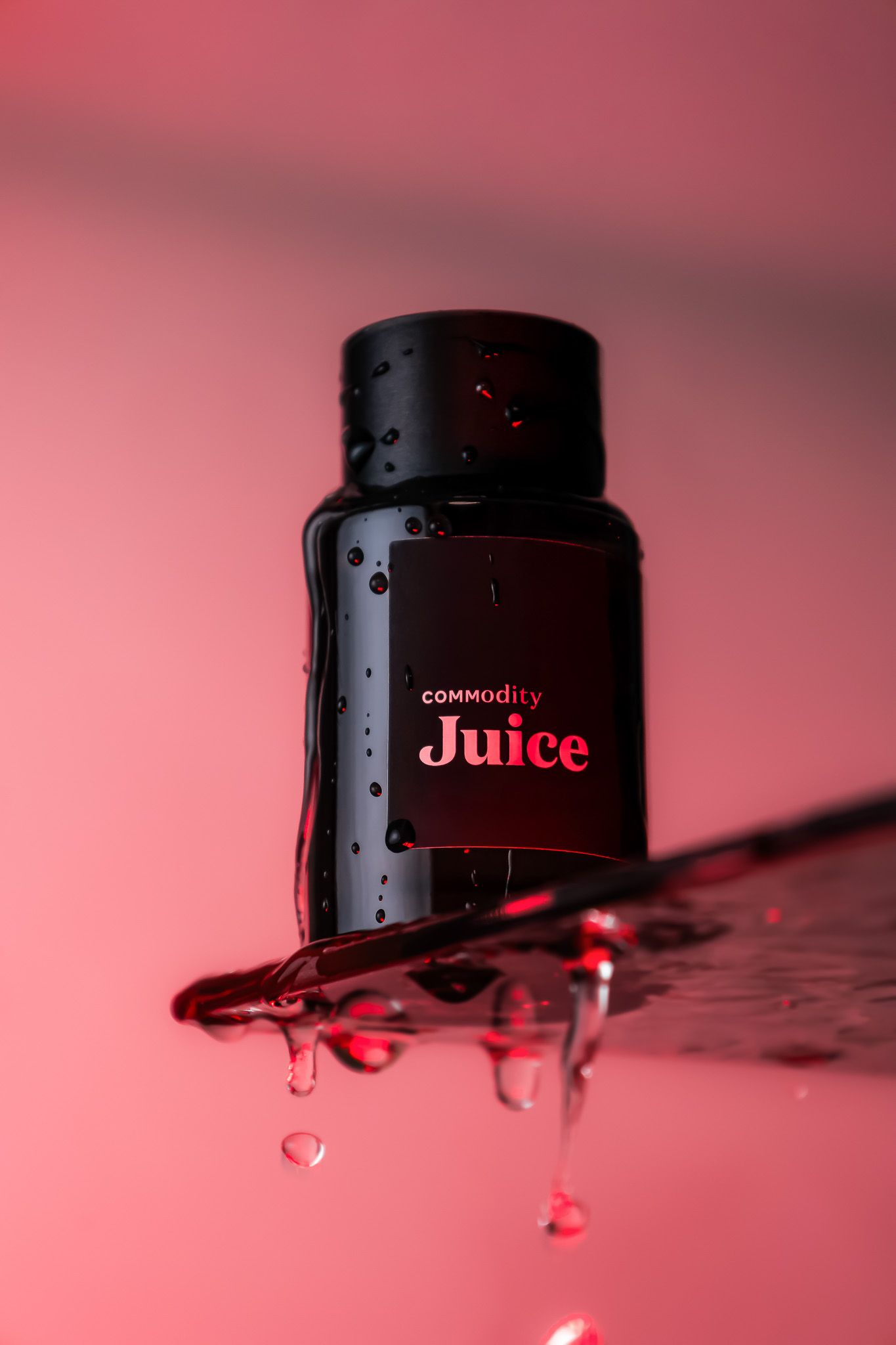 Black cosmetic bottle labeled 'Juice' with water droplets against a pink background.