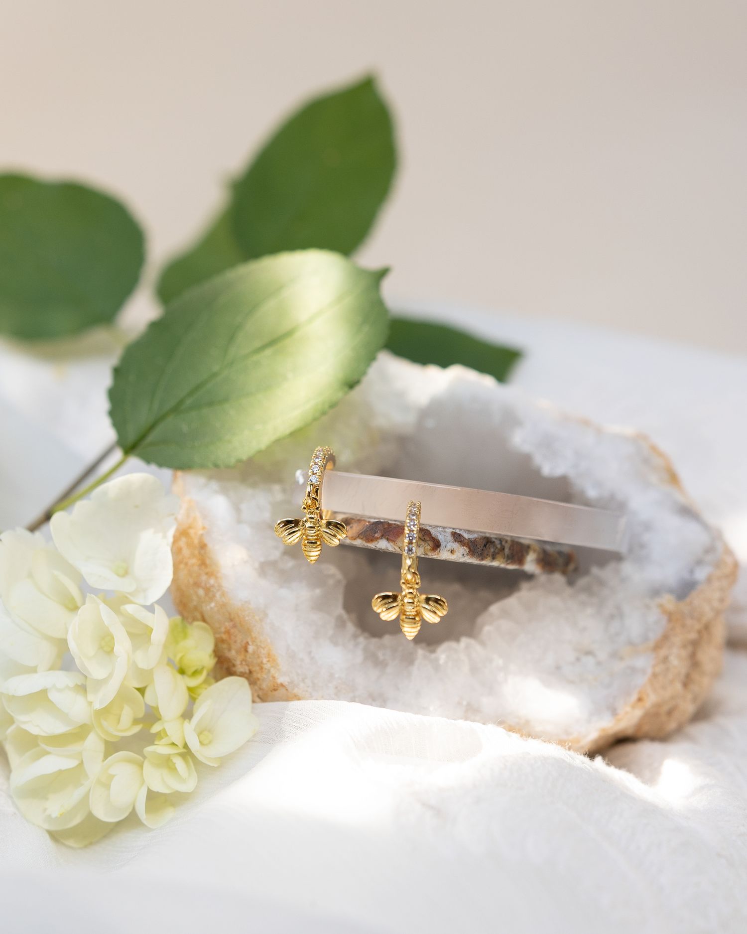 Gold fleur-de-lis earring displayed on crystal geode with white flowers and green leaves.