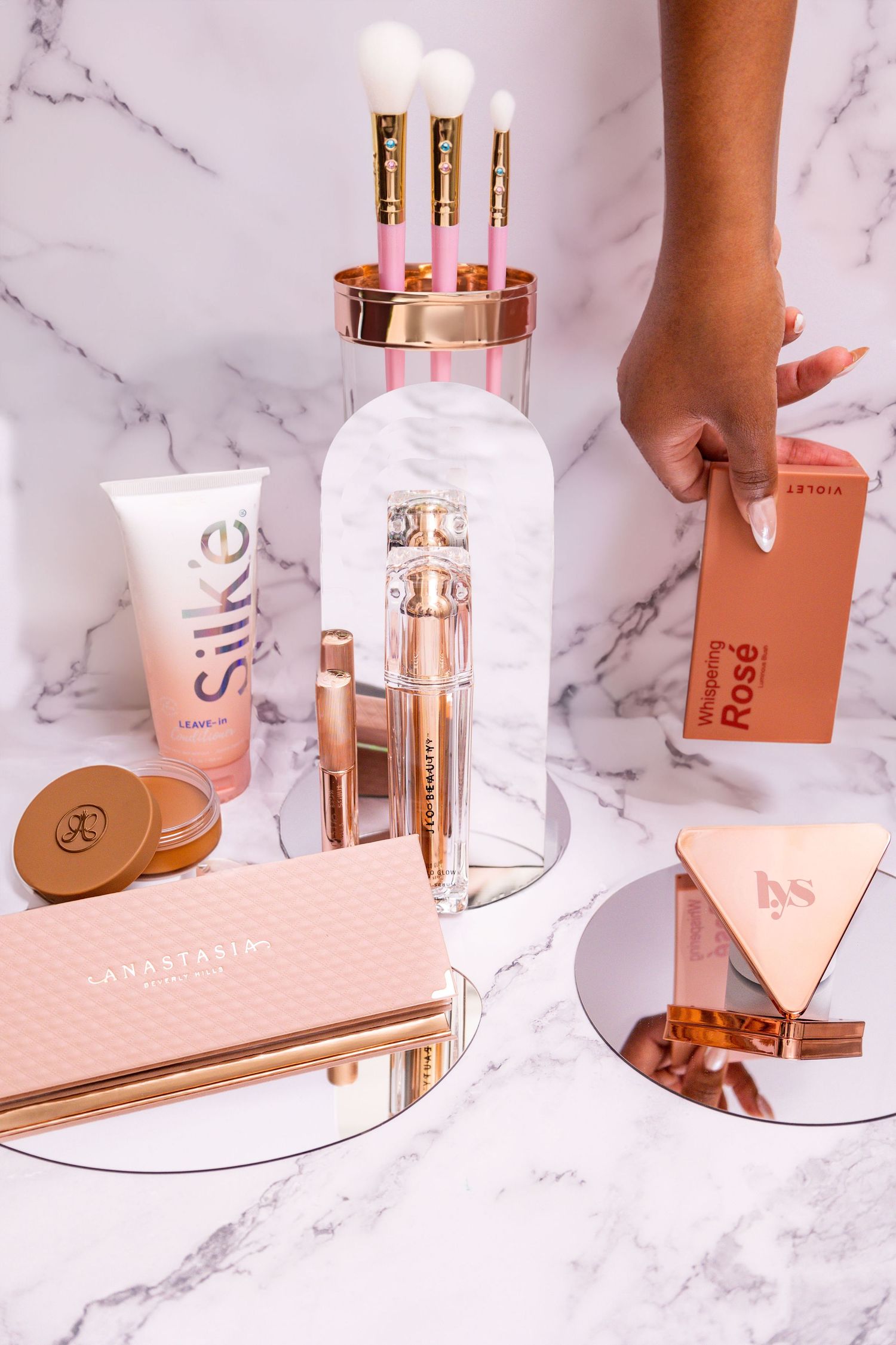 Luxury beauty products with makeup brushes and cosmetics displayed on marble surface with rose gold accents.