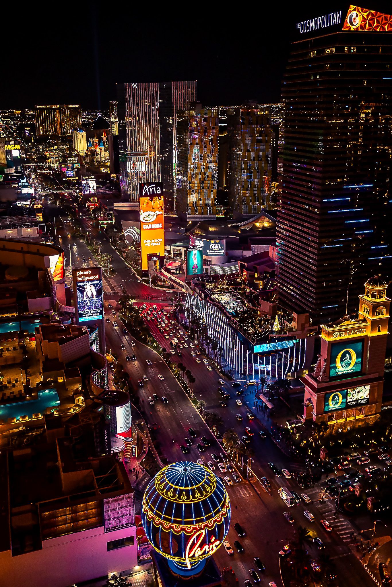 Aerial view of Las Vegas Strip at night showcasing bright neon lights, hotels, and busy streets with traffic.