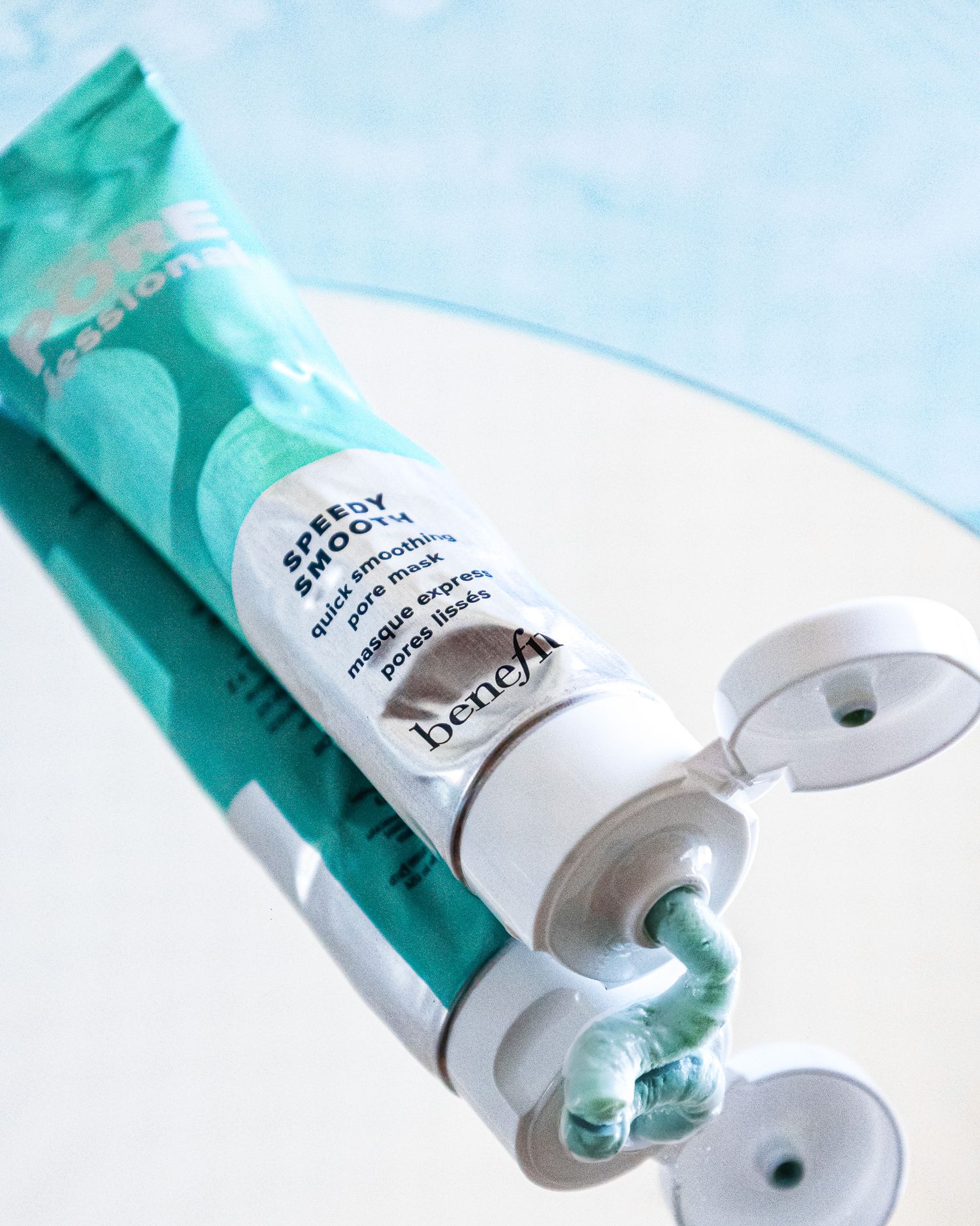 Turquoise skincare product tube with white cream being squeezed out against a light blue background.