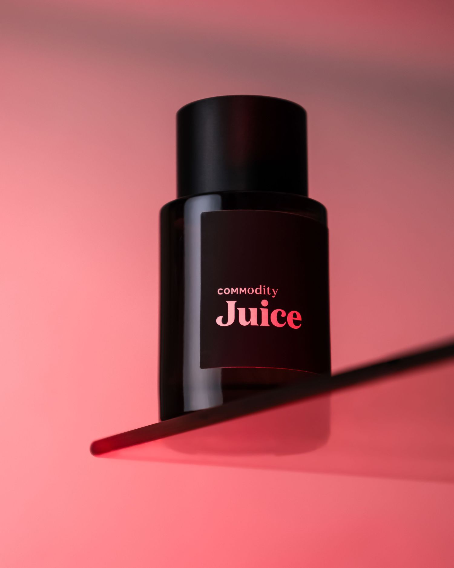Black bottle of Commodity Juice fragrance against pink background with dramatic lighting.