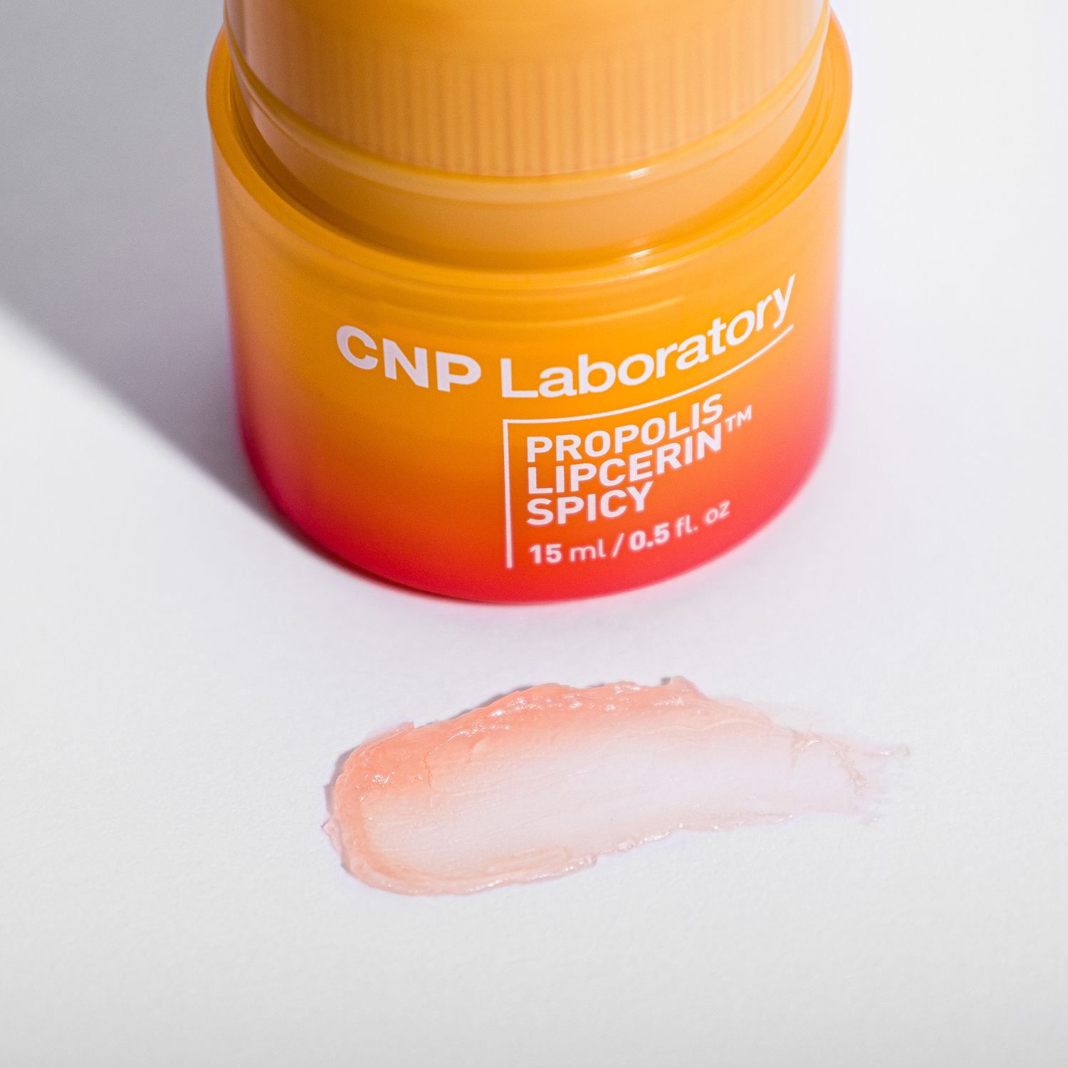 Orange skincare jar from CNP Laboratory with Propolis Lip serum product and a peach-colored swatch sample on display.