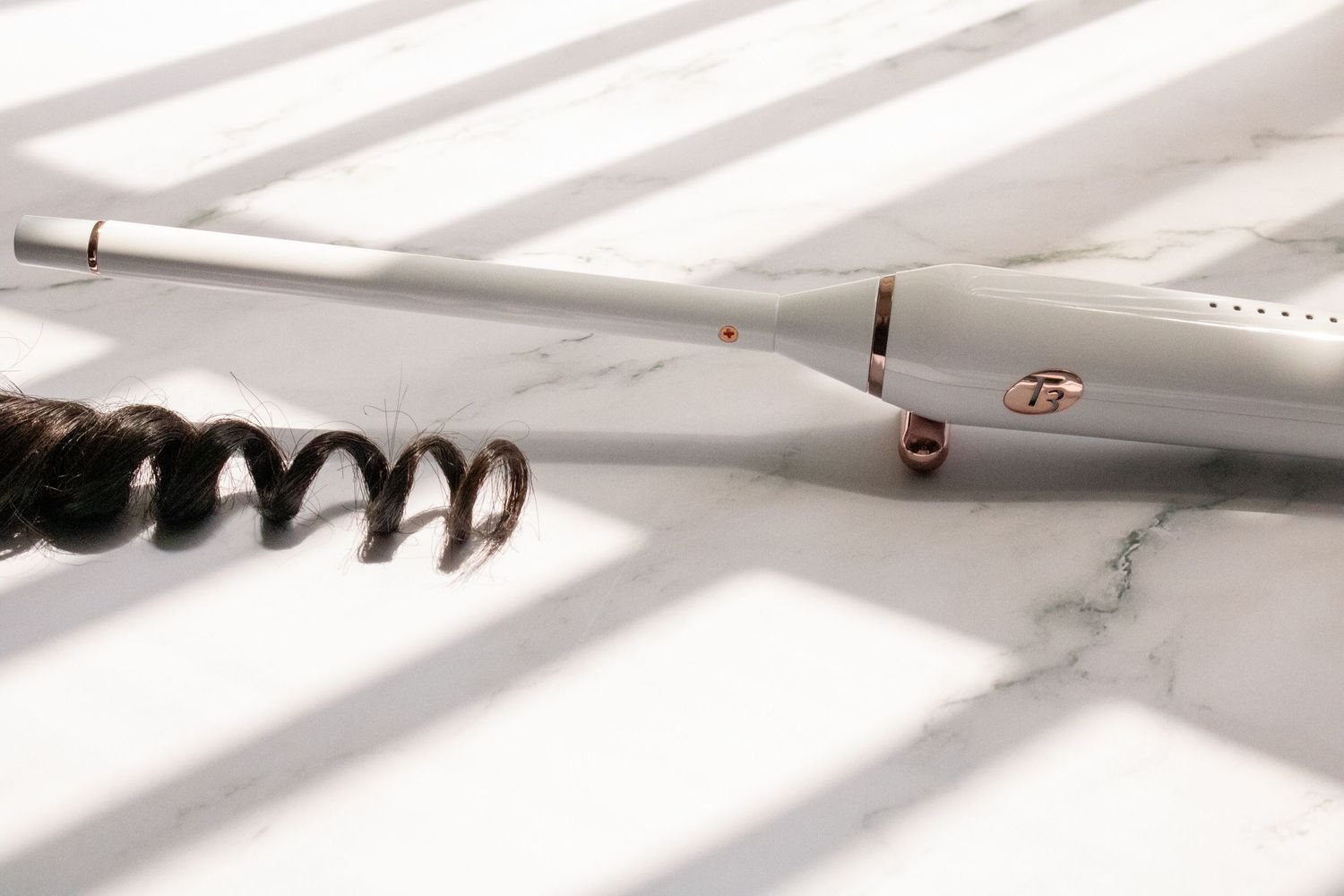White curling iron on marble surface with shadows creating striped pattern.