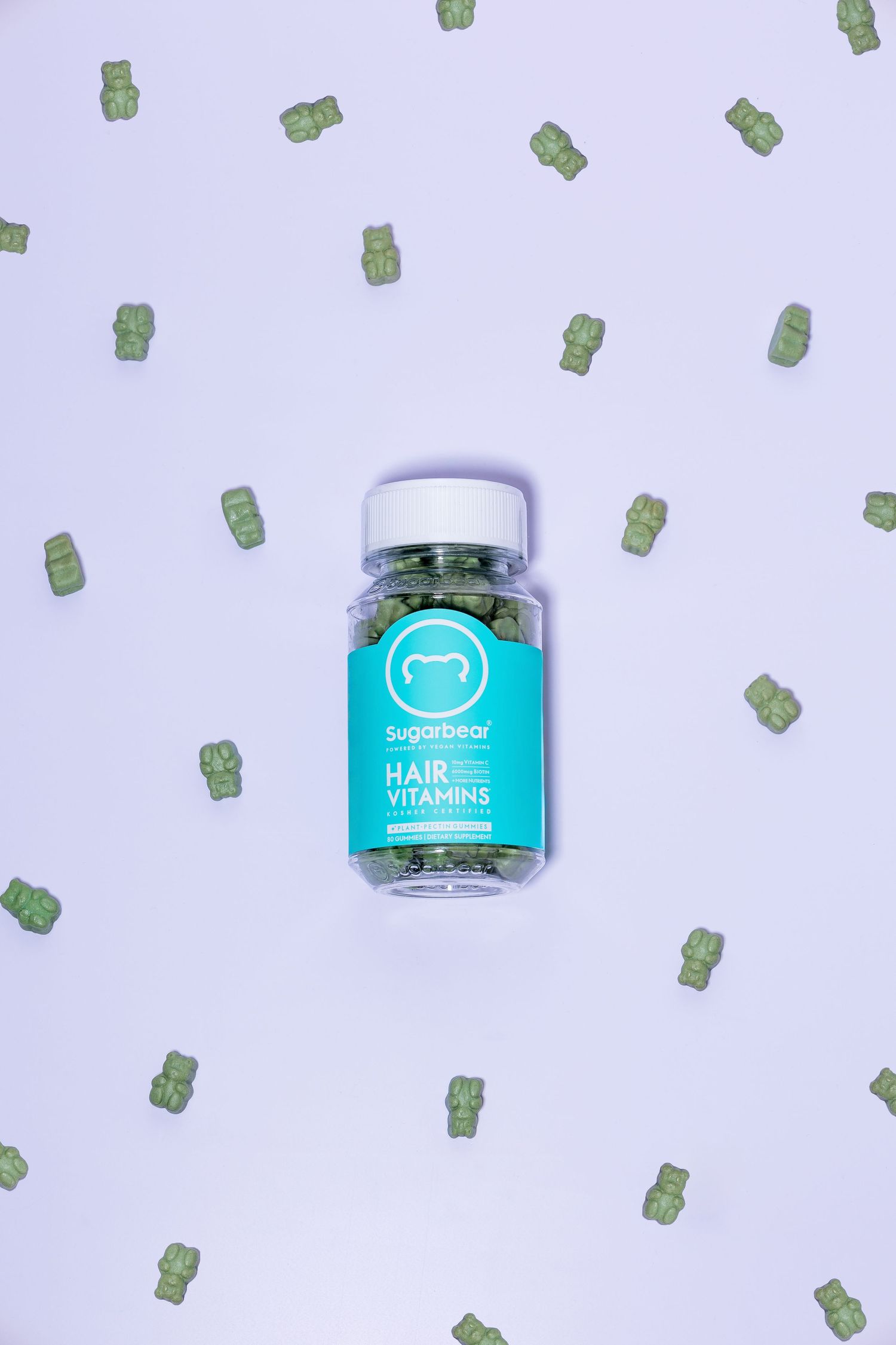 Hair vitamin gummy supplement bottle on purple background with scattered gummy bears.