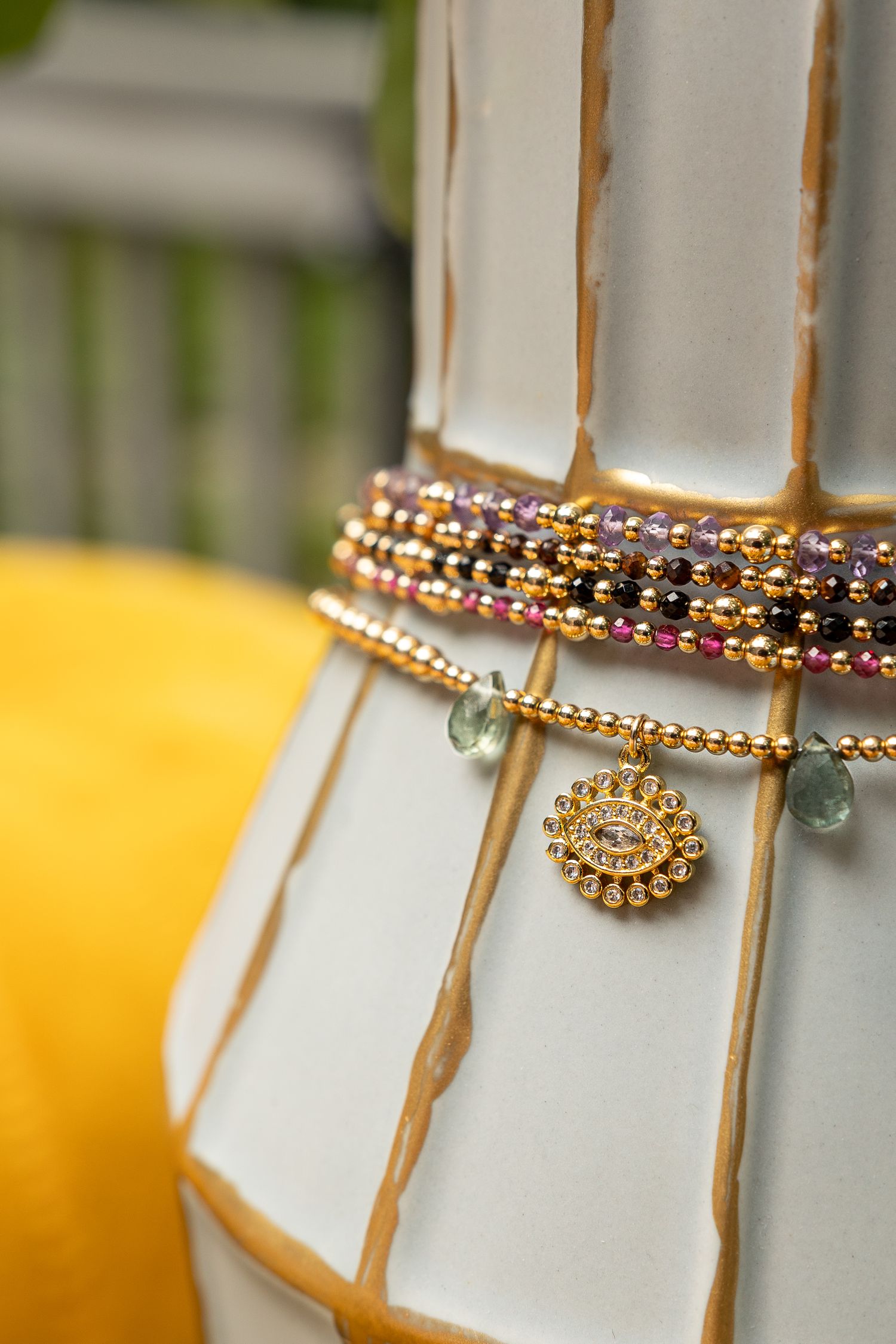 Close up of stacked beaded bracelets and gold pendant displayed on white surface.
