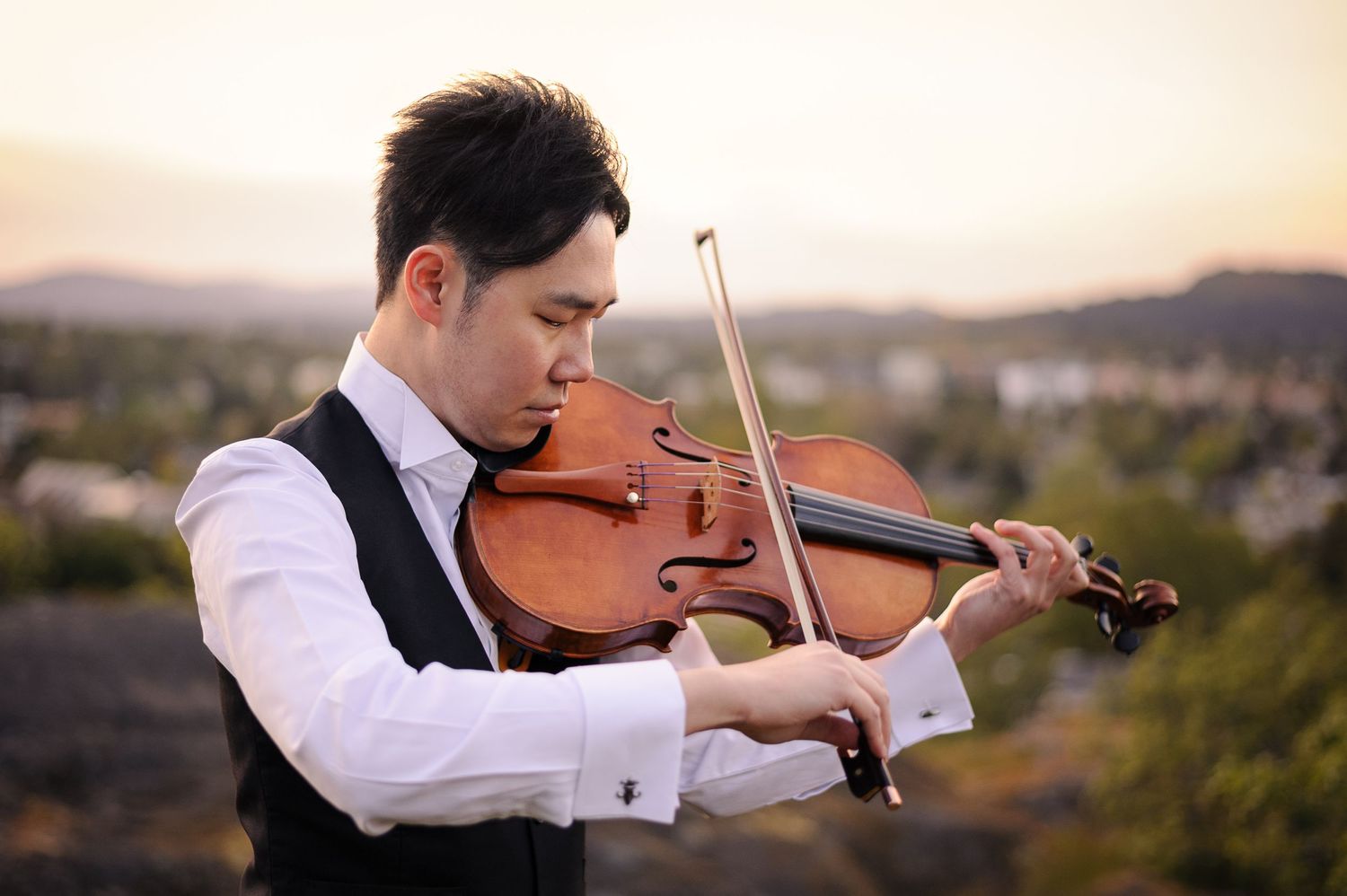 A man in an elegant vest playing viola against a mountain sunset.