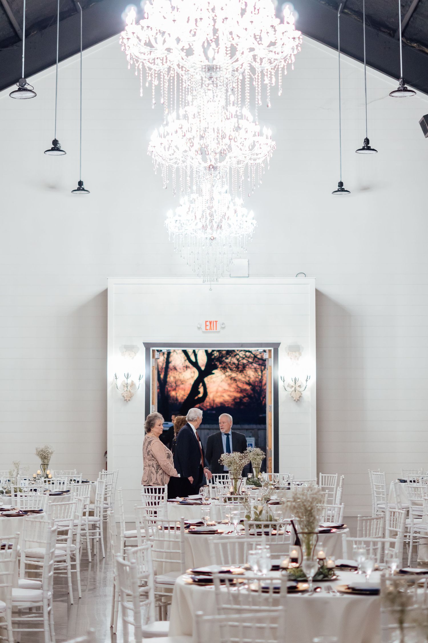 An elegant white reception venue with crystal chandeliers and white chiavari chairs.