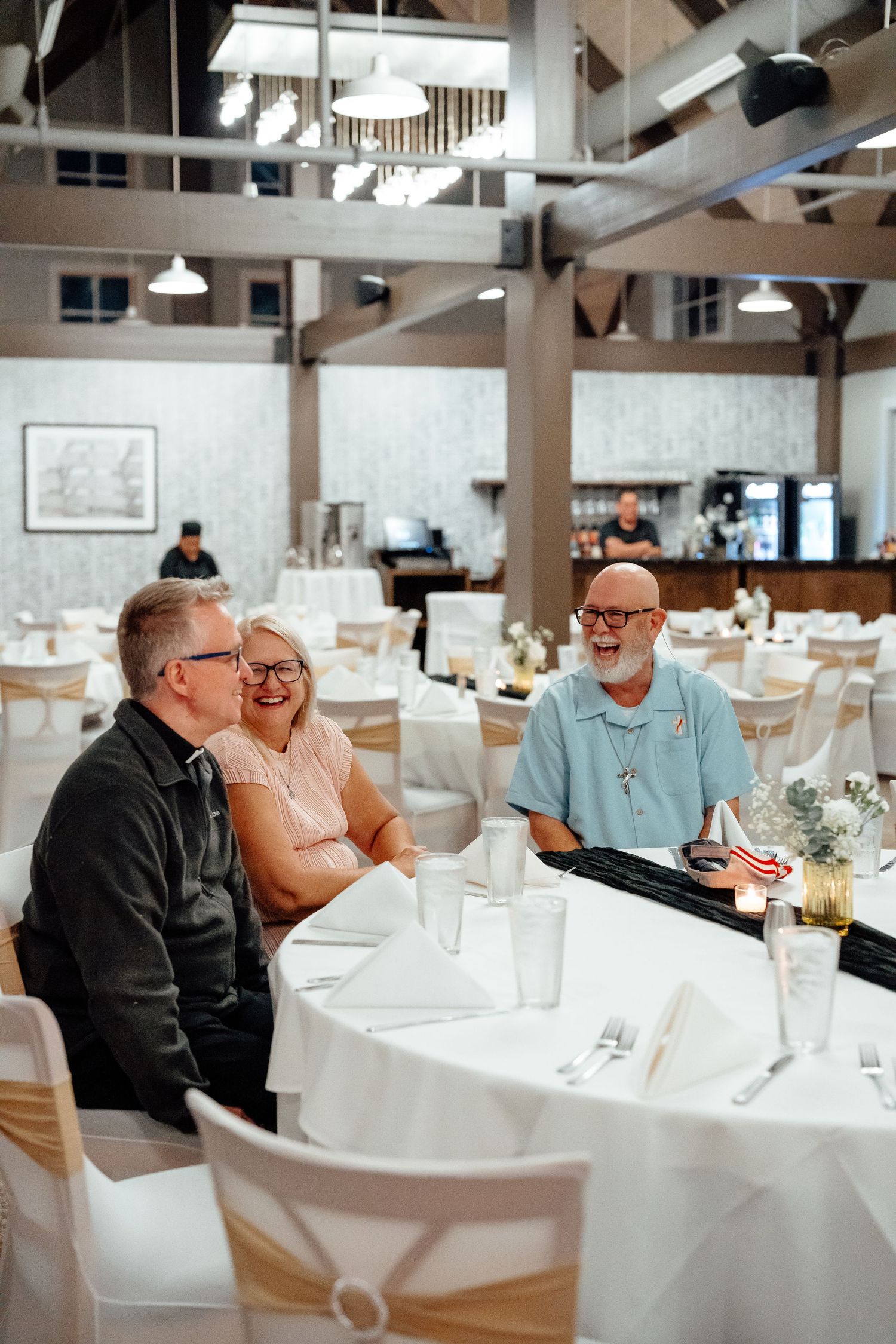 People enjoying a celebratory dinner at tables decorated with white linens in a bright venue.