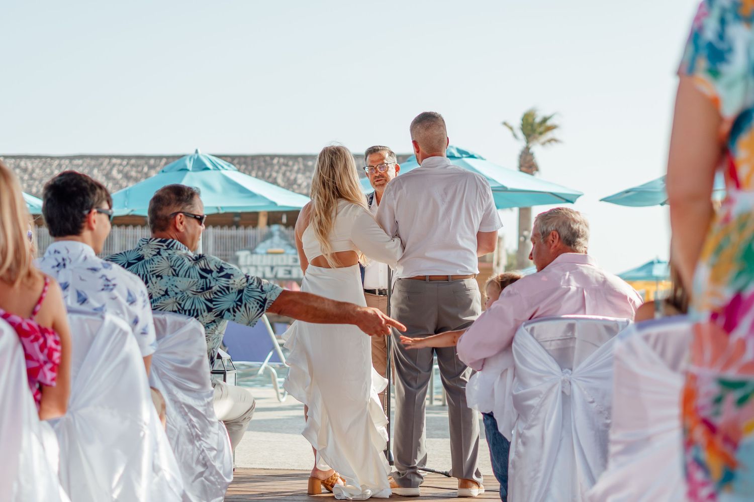 Wedding celebration on a tropical beach with white chairs and decorations.