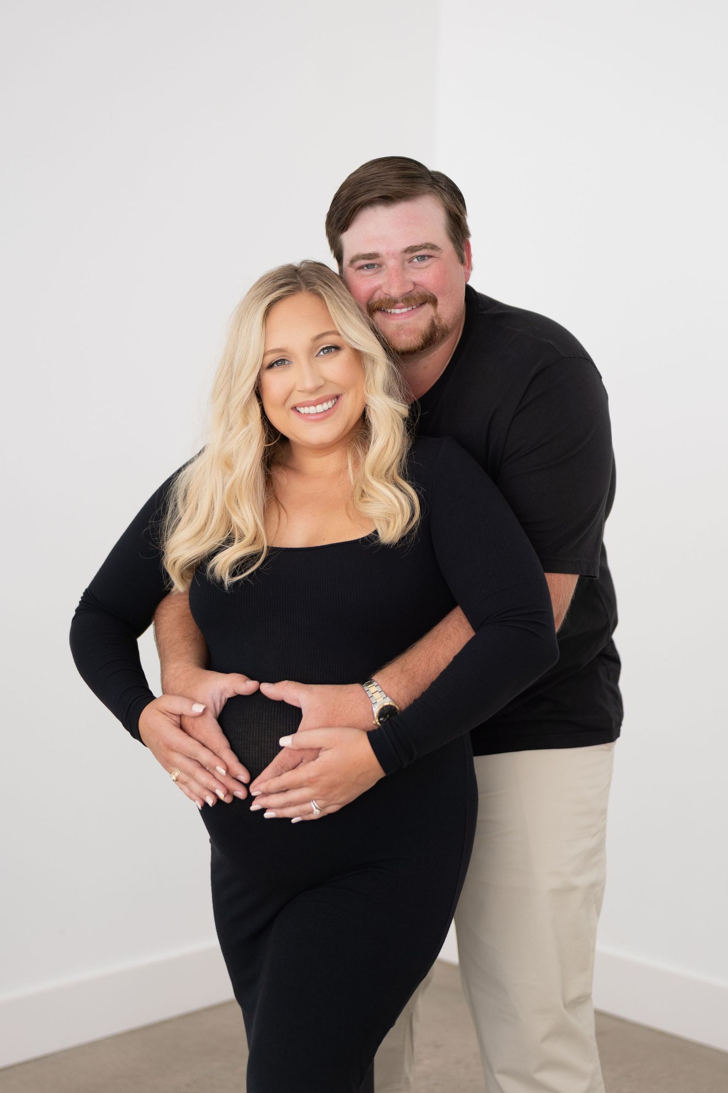 Maternity photoshoot showing couple embracing against white background.