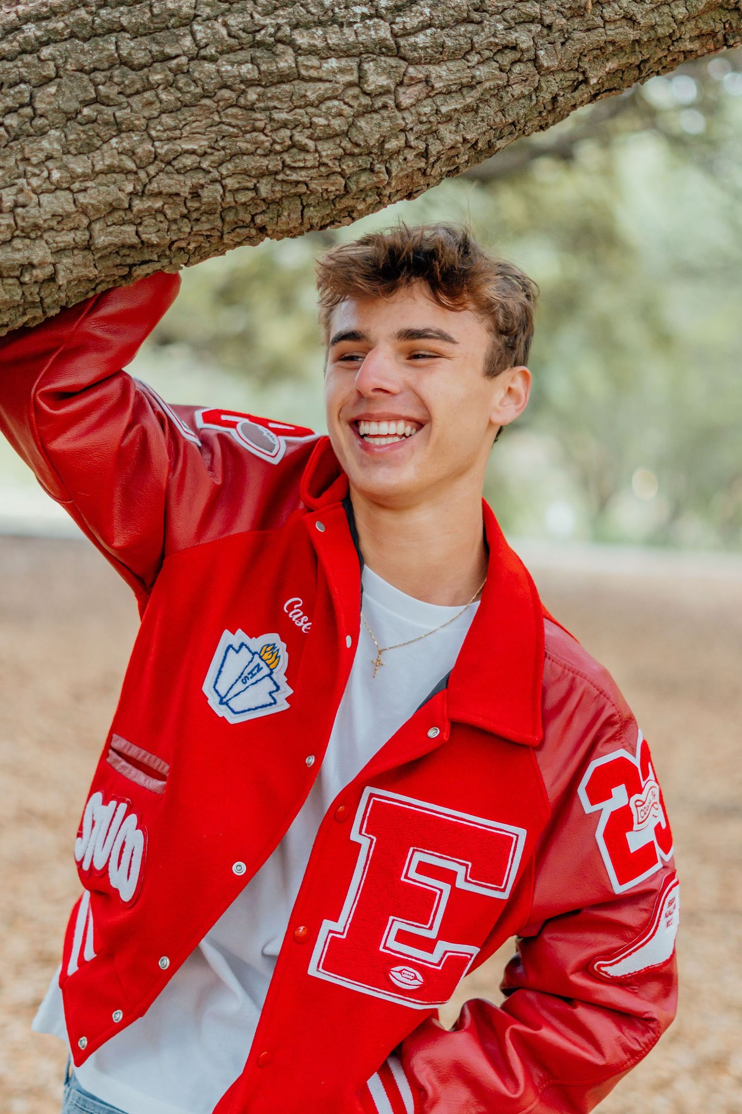 Portrait of person in red varsity jacket smiling under tree branch.