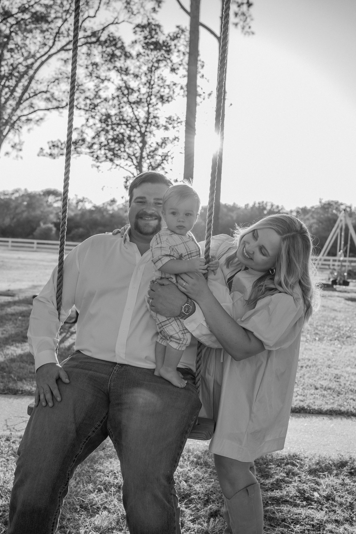 A family poses together on a swing set in a black and white outdoor portrait.