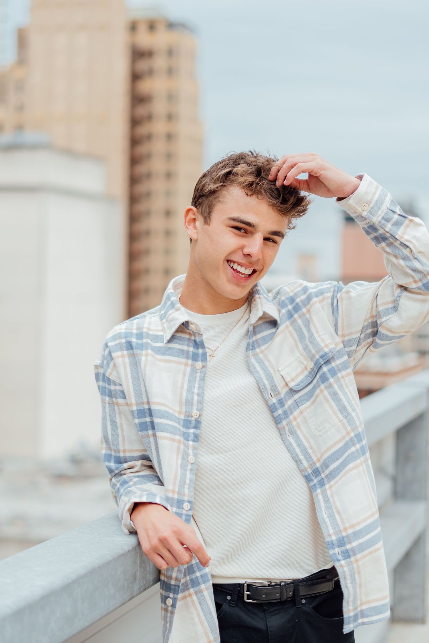 Portrait of person in plaid button-down shirt smiling on urban rooftop.