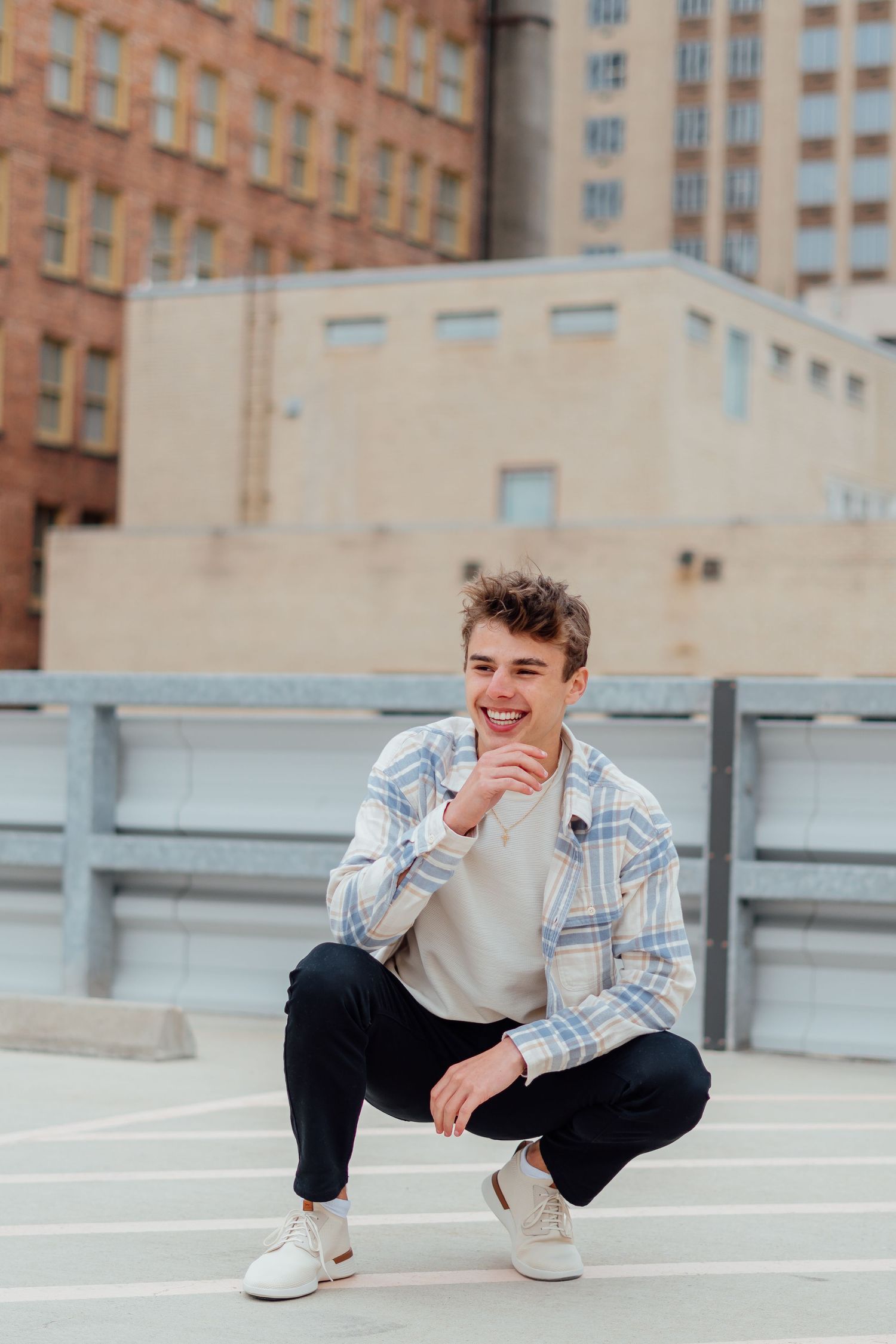 Urban portrait of person in plaid jacket crouching on concrete surface.