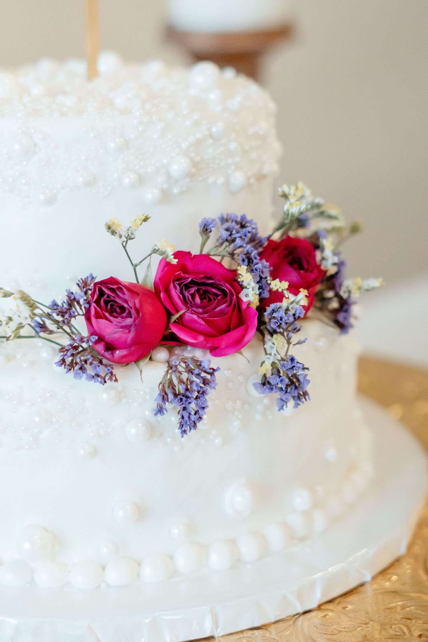 Wedding cake decorated with fresh pink roses and purple flowers on a white frosted surface.