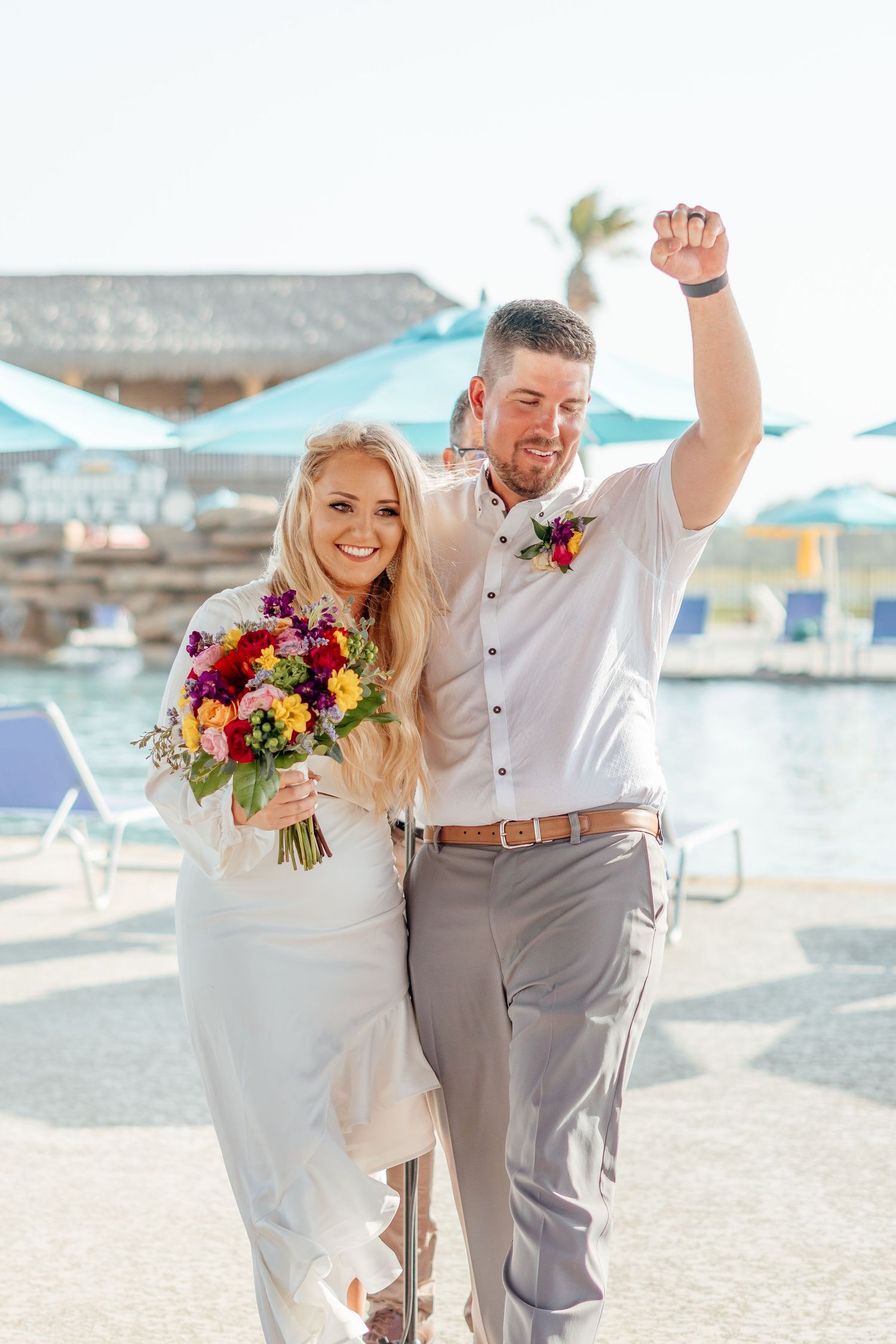 Newlyweds celebrating on a sunny beach with vibrant bouquet and ocean backdrop.