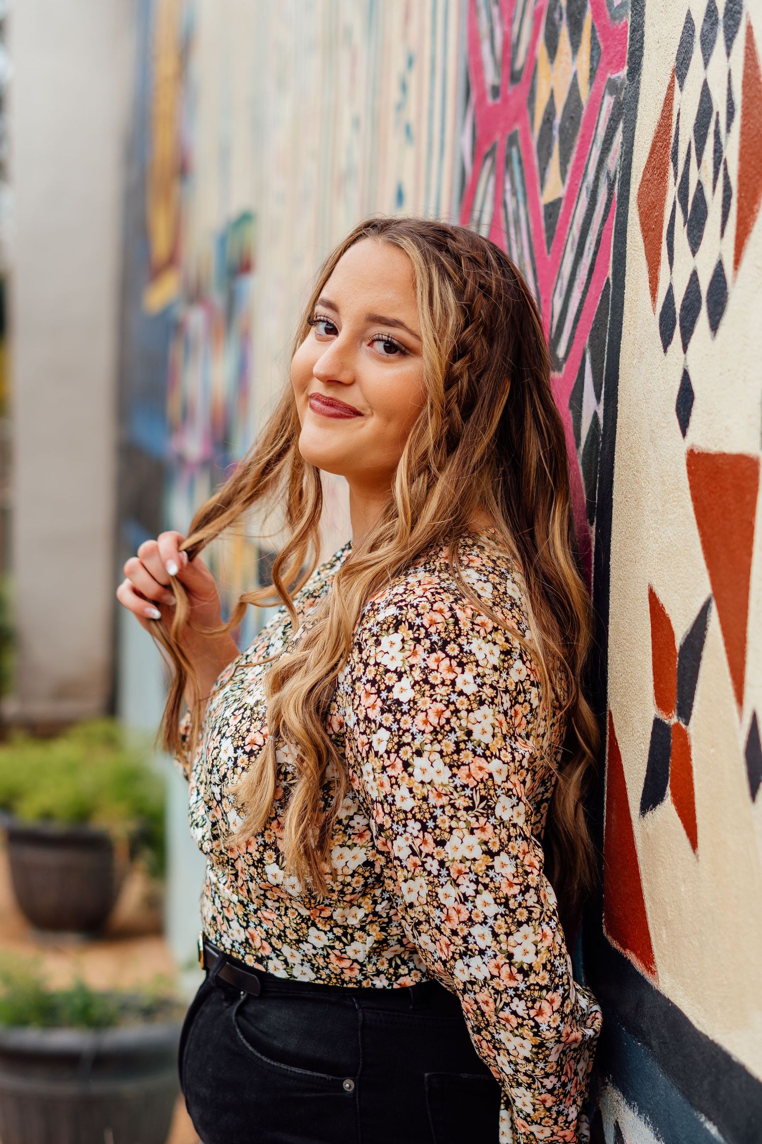 Portrait against a colorful mural wall wearing a floral print top and dark bottoms.