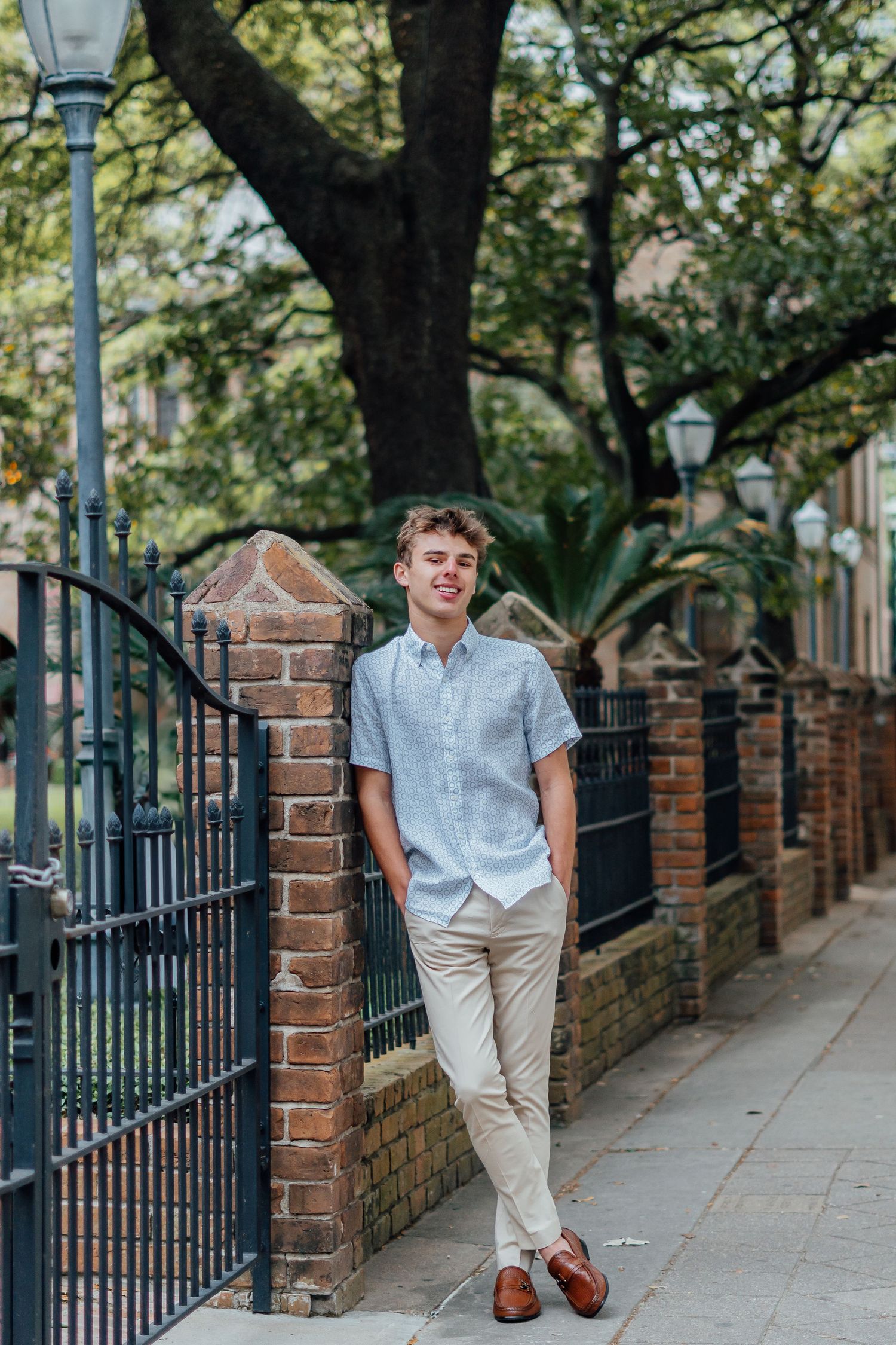 Portrait of person in casual attire leaning against brick wall with iron fence.