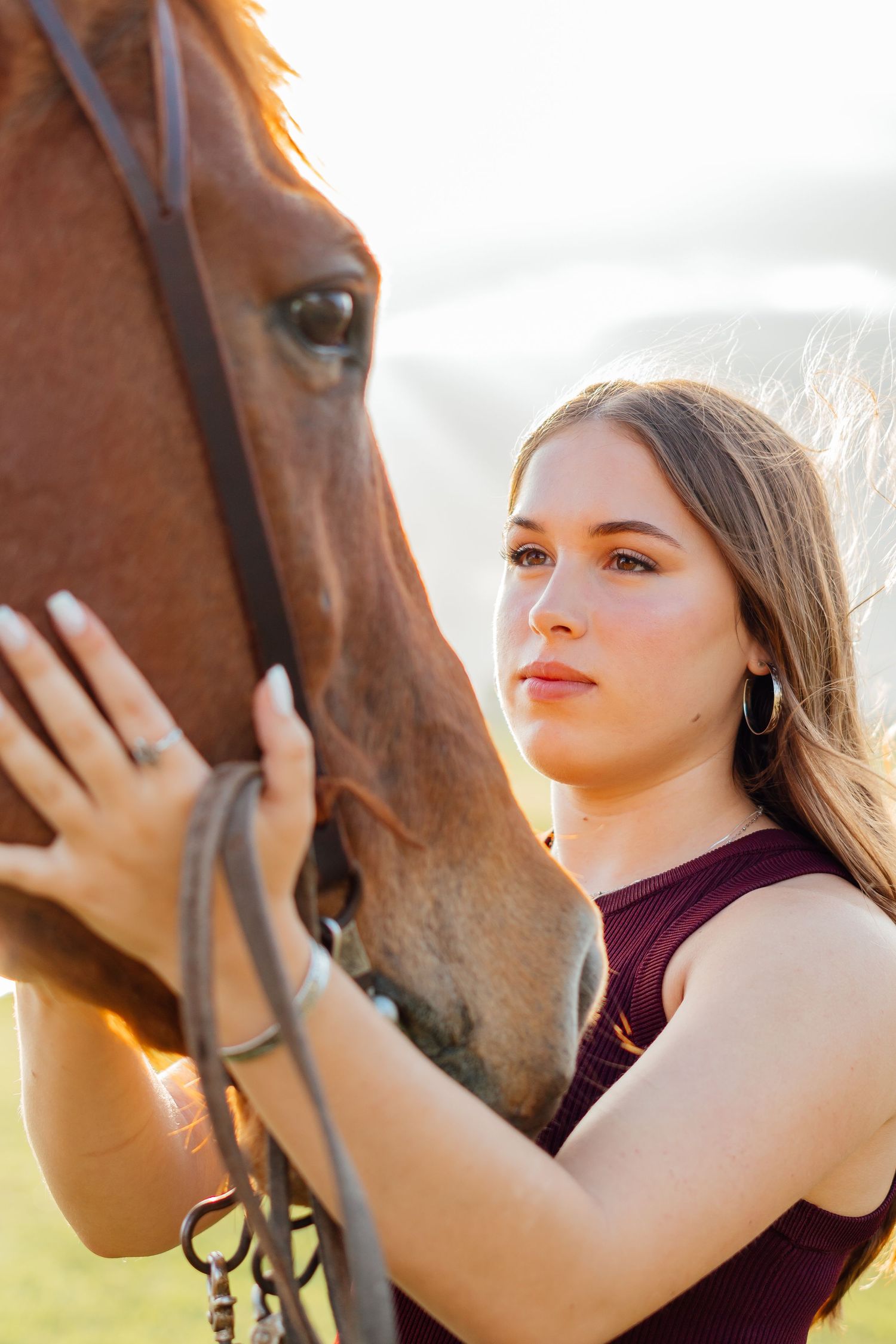 A close-up portrait of someone posing with a brown horse against a sunlit outdoor background.