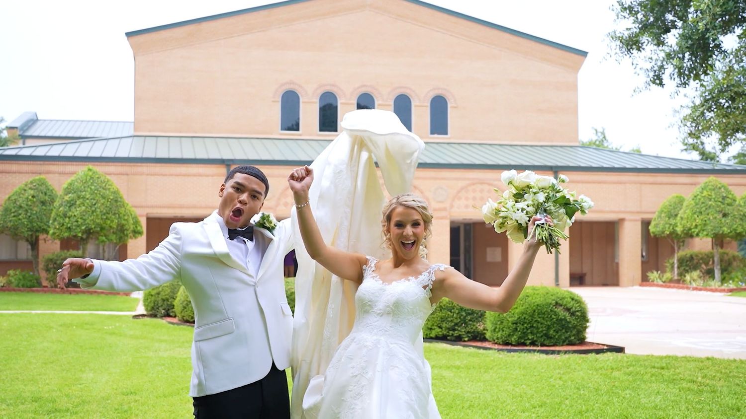 A wedding couple poses joyfully outside a church building with white columns.