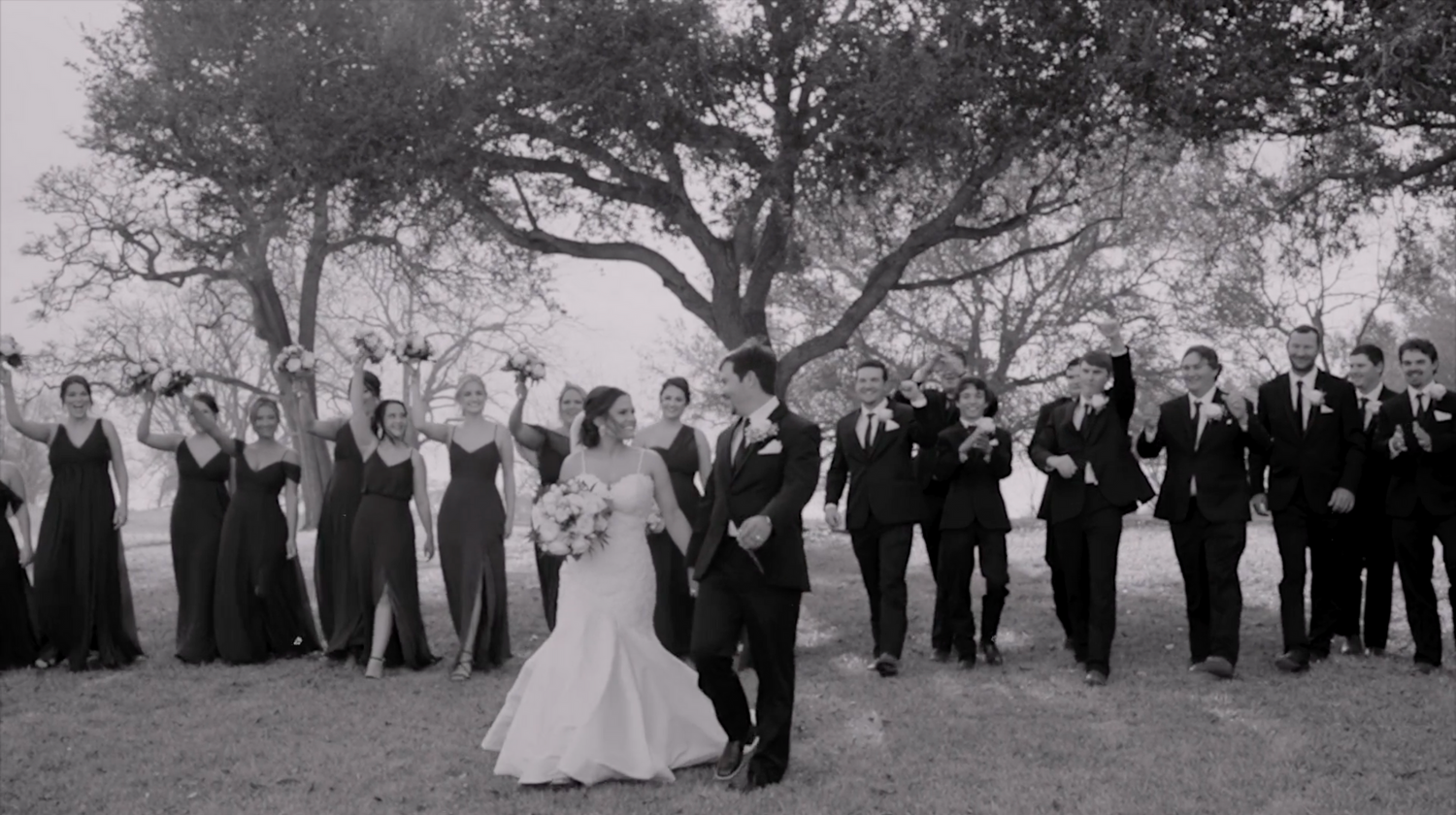 Wedding party group shot outdoors with trees and natural scenery in the background.