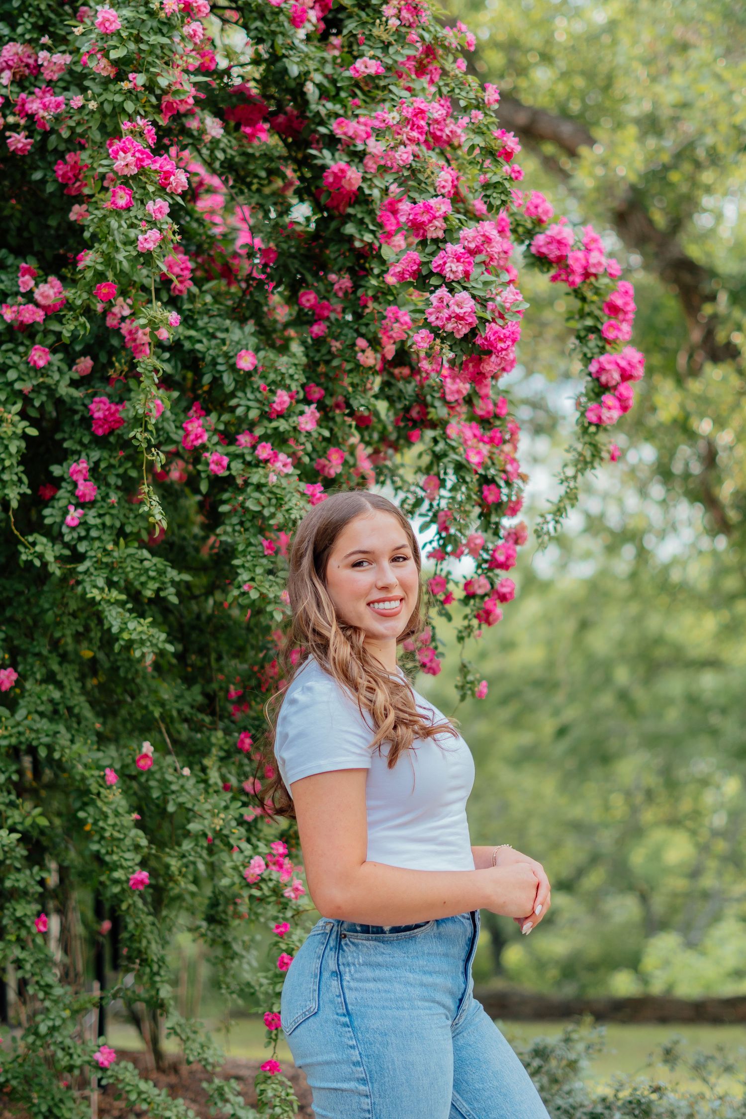 A photoshoot in front of blooming pink rose bushes featuring casual denim style.