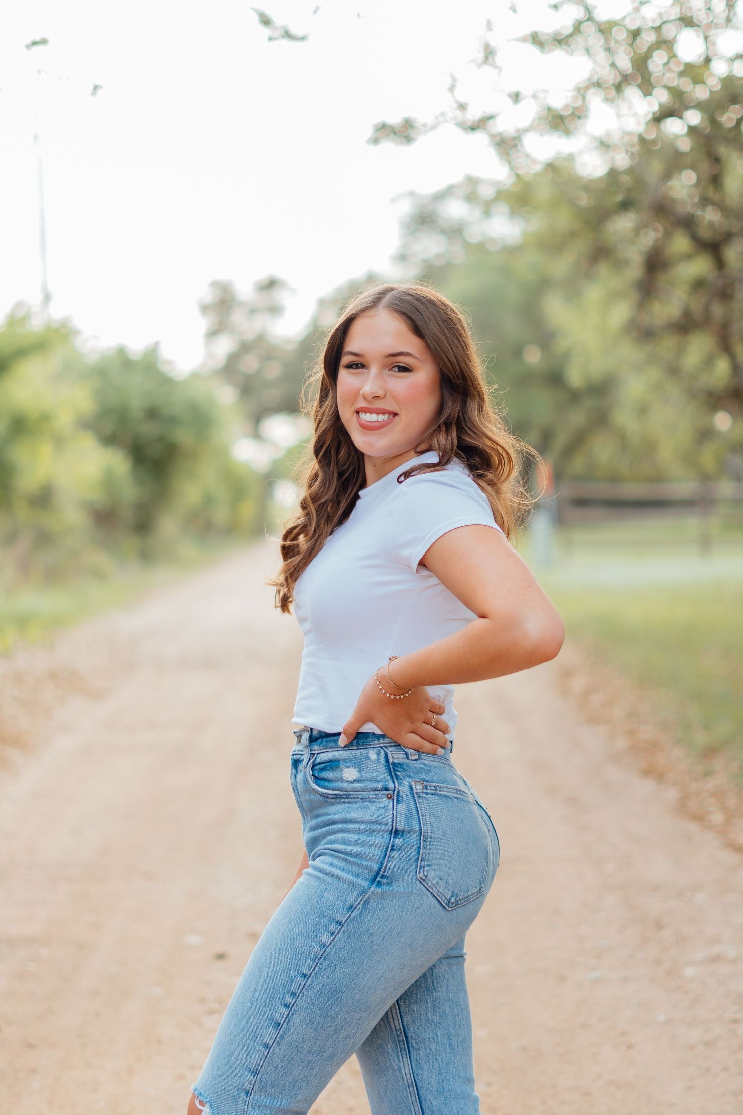 Someone poses in casual denim outfit on a rural dirt path during a golden hour photoshoot.