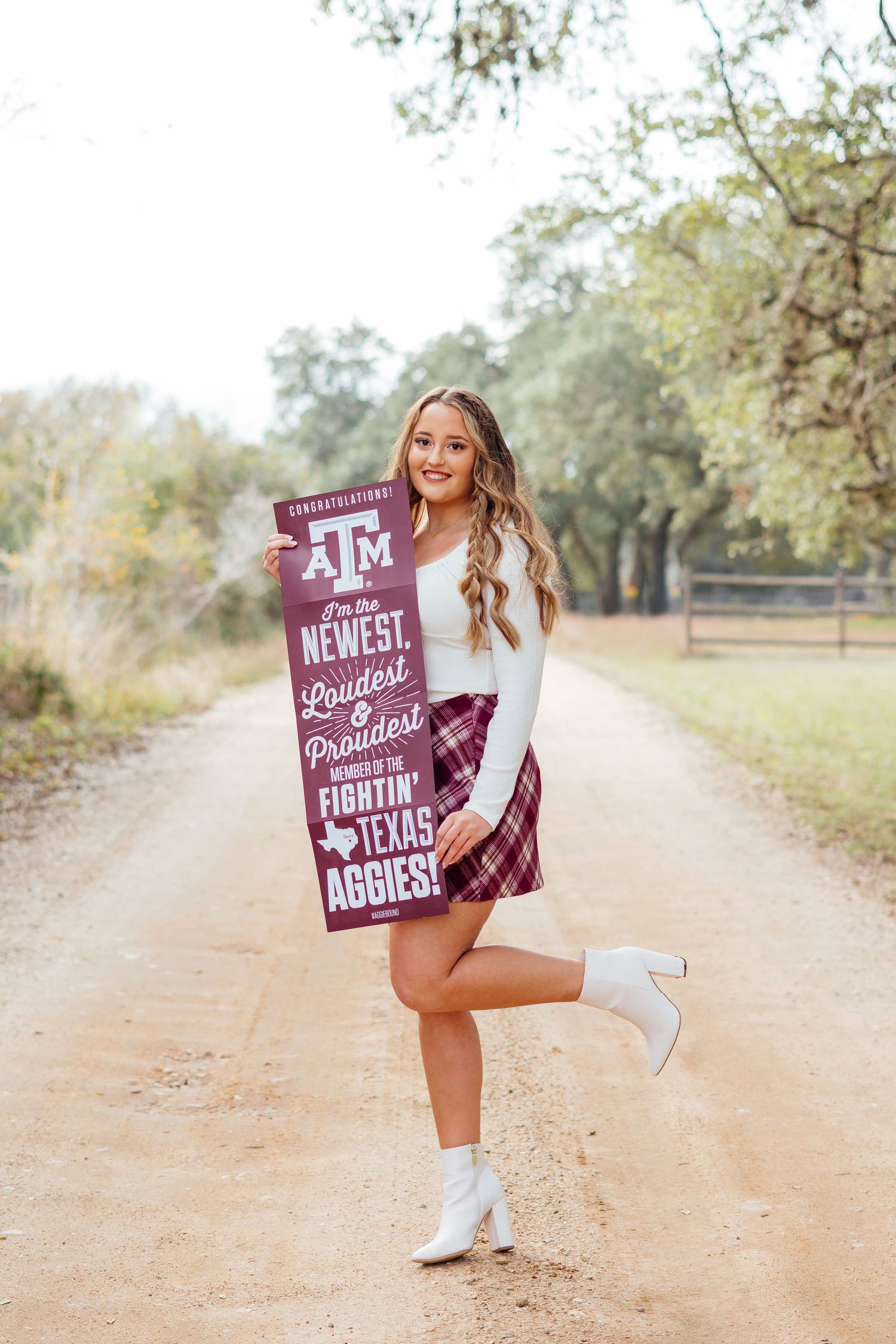Casual portrait on dirt path with Texas A&M sign and white boots against autumn backdrop.