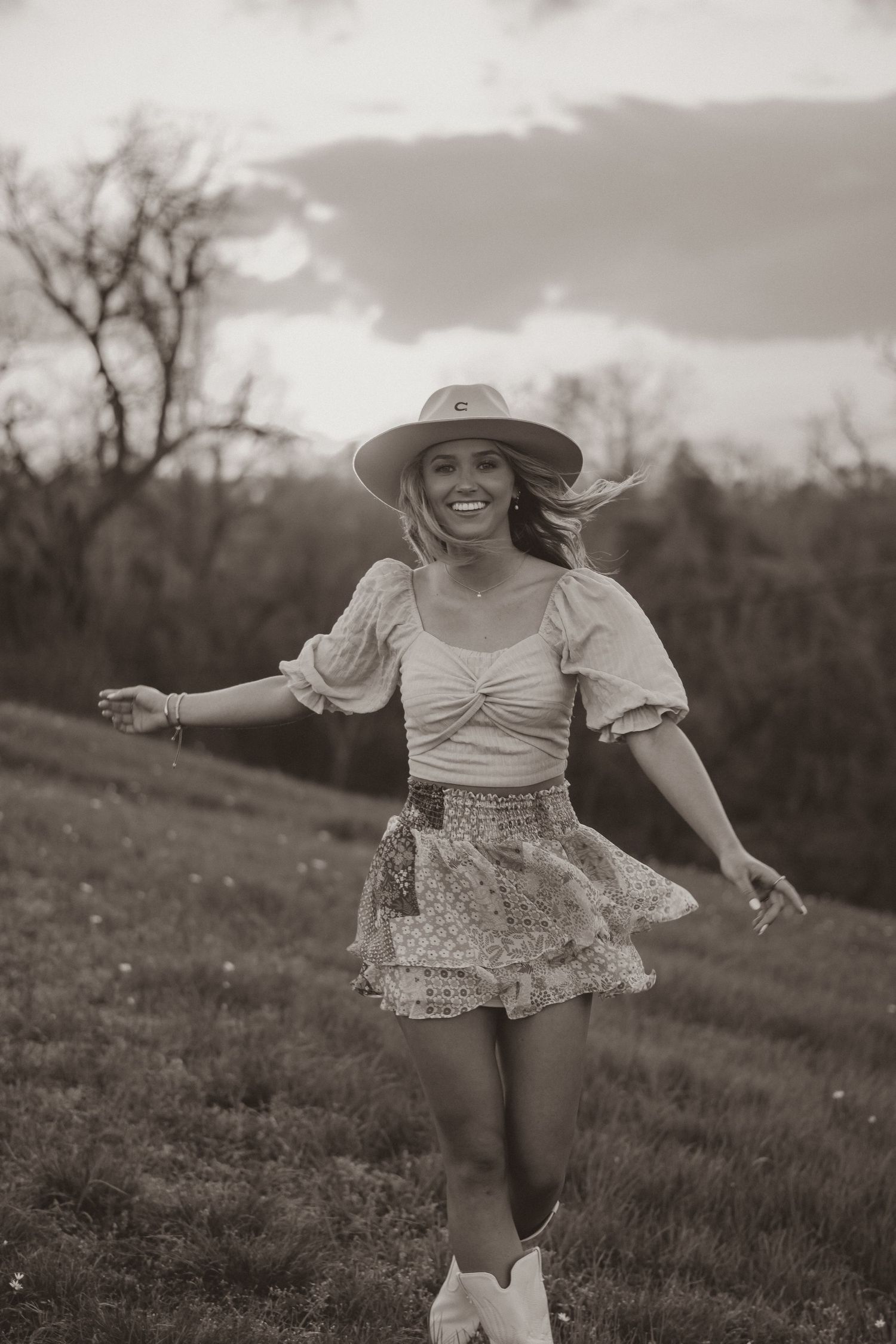 Black and white portrait of joyful dancing in ruffled skirt and western hat.