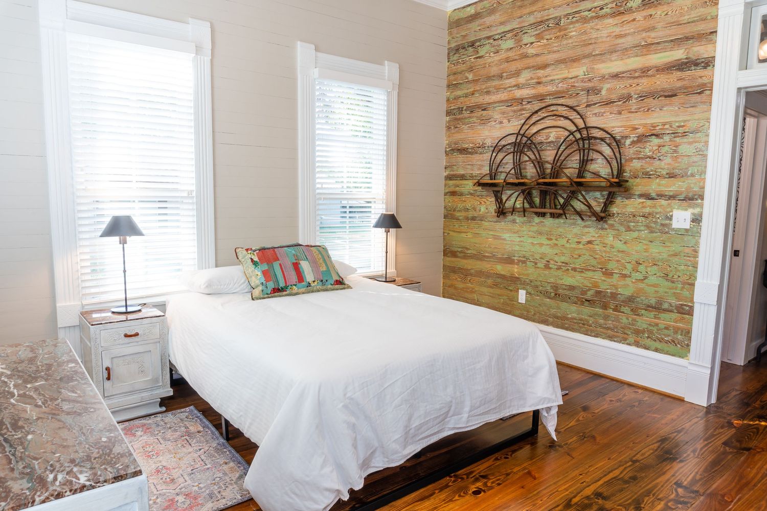 Cozy bedroom with rustic wood accent wall, white linens and natural lighting.