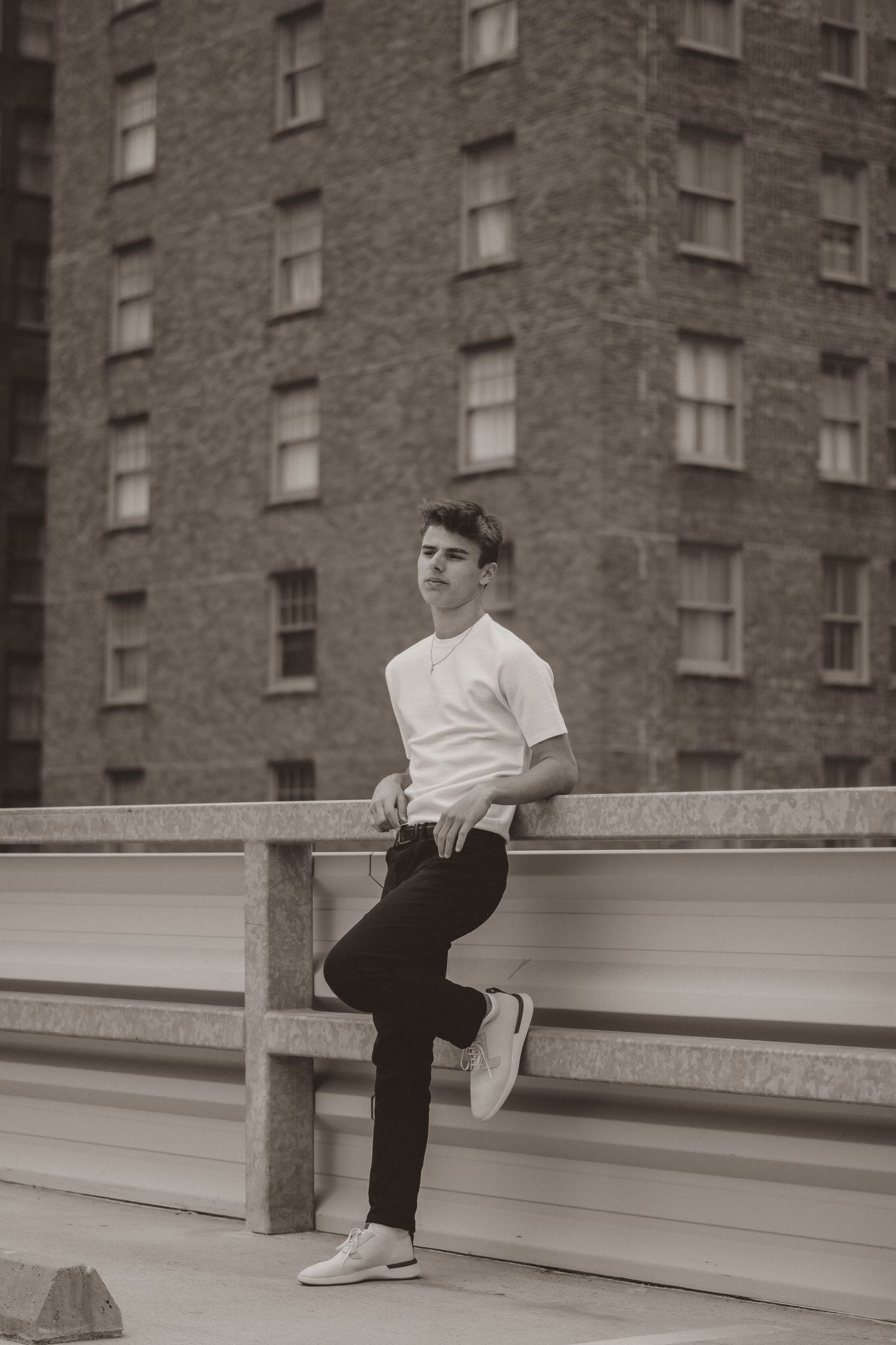 Vintage-style portrait of person in white t-shirt leaning on railing with brick building behind.
