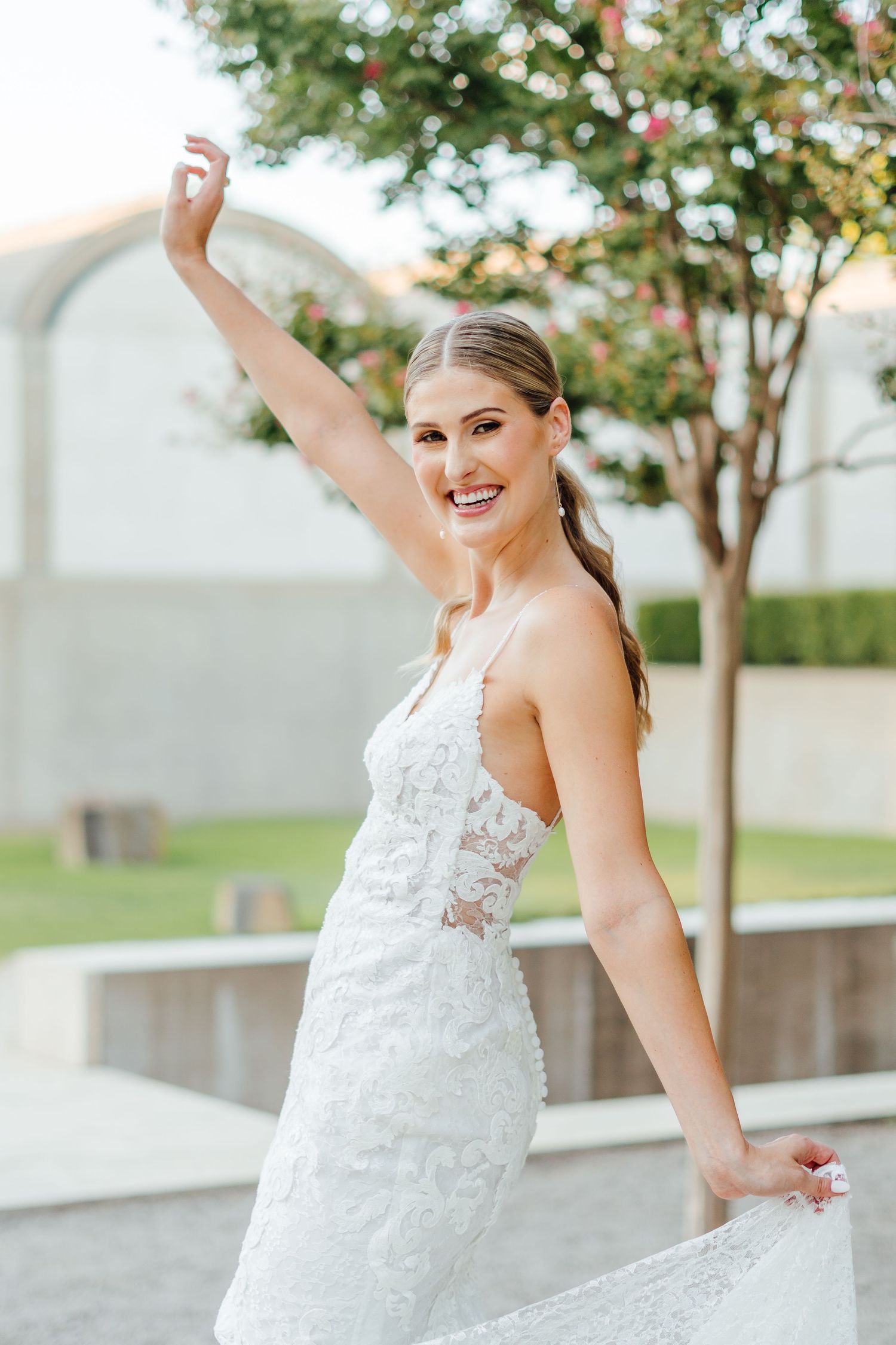 Joyful bridal portrait with flowing lace dress against modern architectural background.