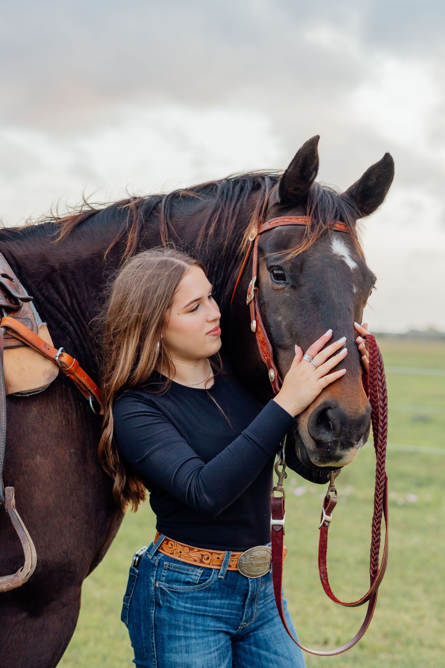 Person wearing black top embraces dark brown horse in grassy field.