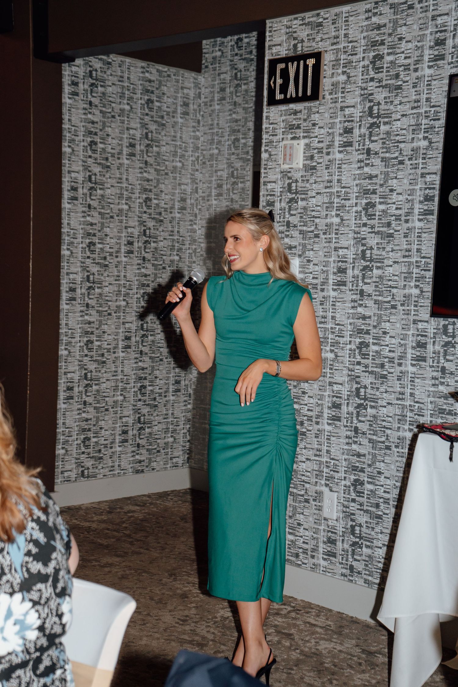 Woman in teal dress speaking at podium during formal event.