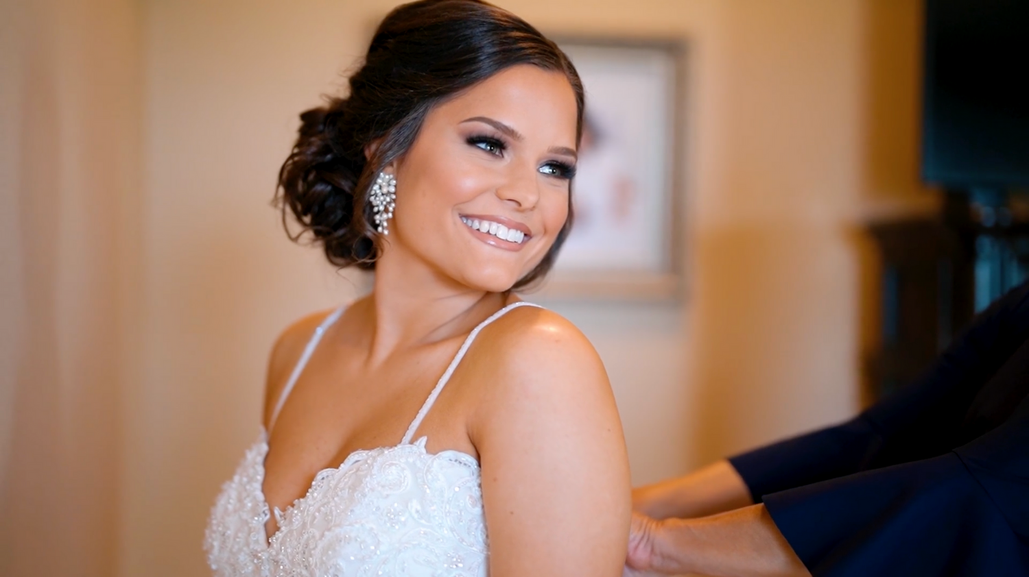 Bride in an elegant white strapless gown poses with dramatic window lighting in a luxurious room.