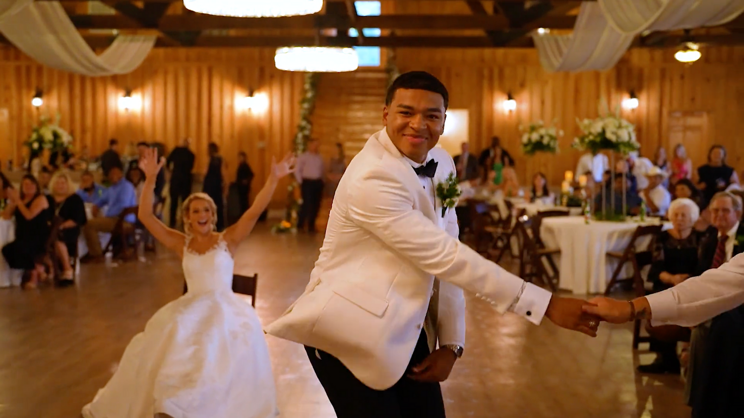 Wedding reception venue with warm lighting and rustic wooden beams overhead.