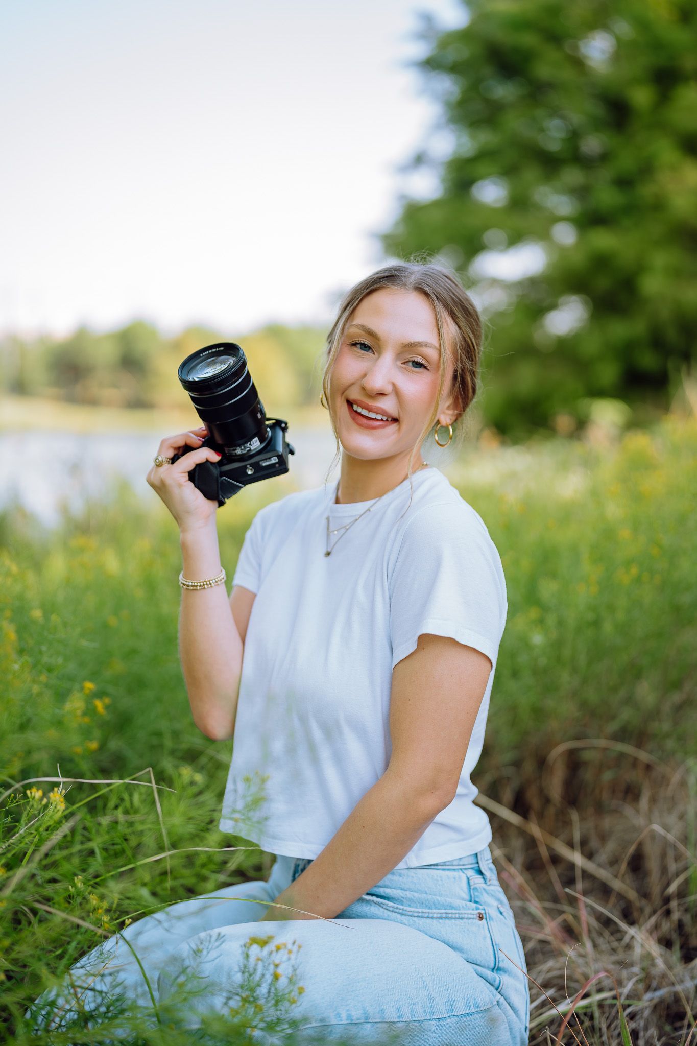 Person in casual attire holding a camera while sitting in a summer meadow.